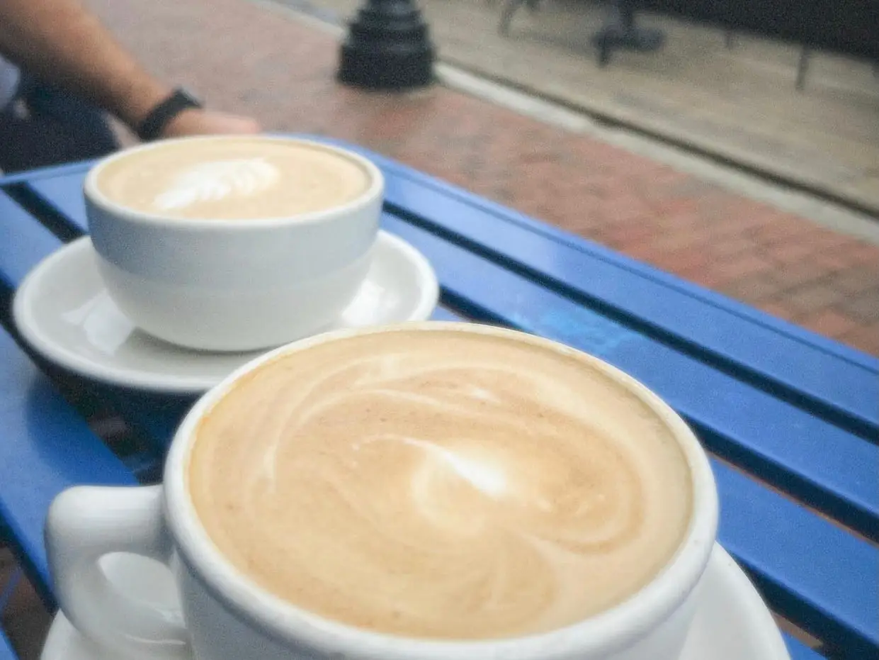Two cappuccinos on a blue picnic table.