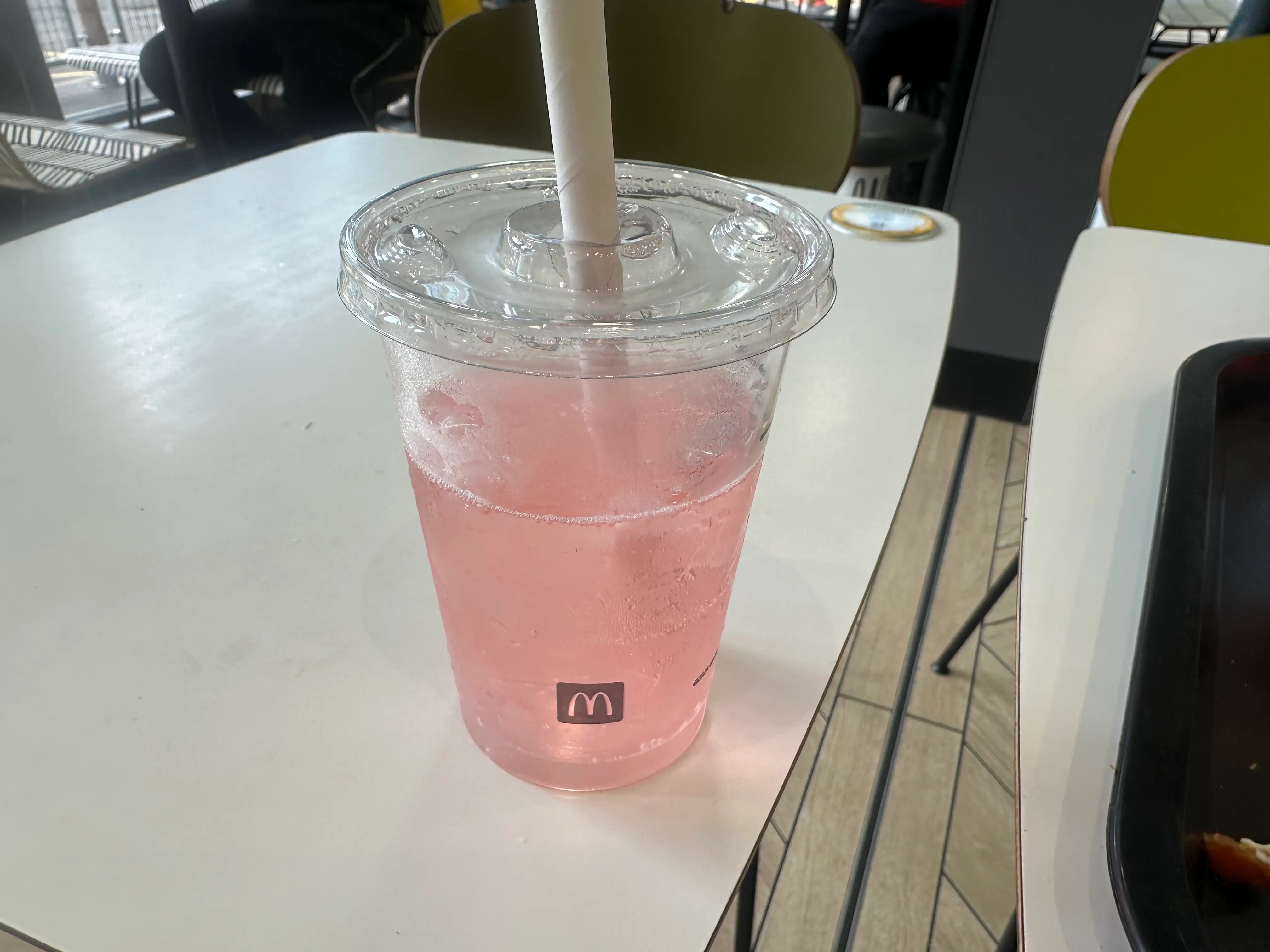 Pink iced drink in a clear McDonald's cup with a straw on a restaurant table.