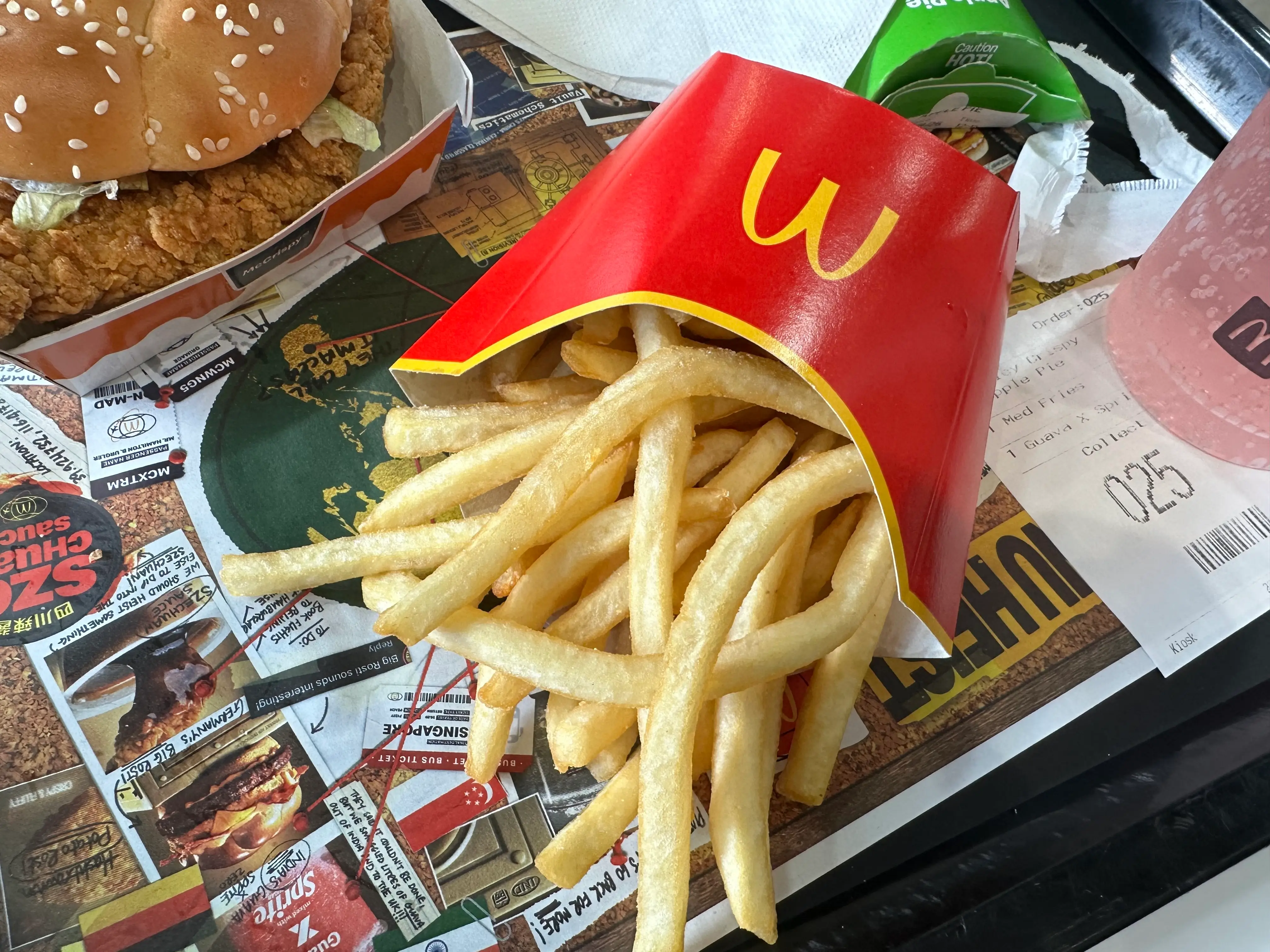 McDonald's fries in a red carton sit on a tray beside a chicken sandwich, receipt, and drink.