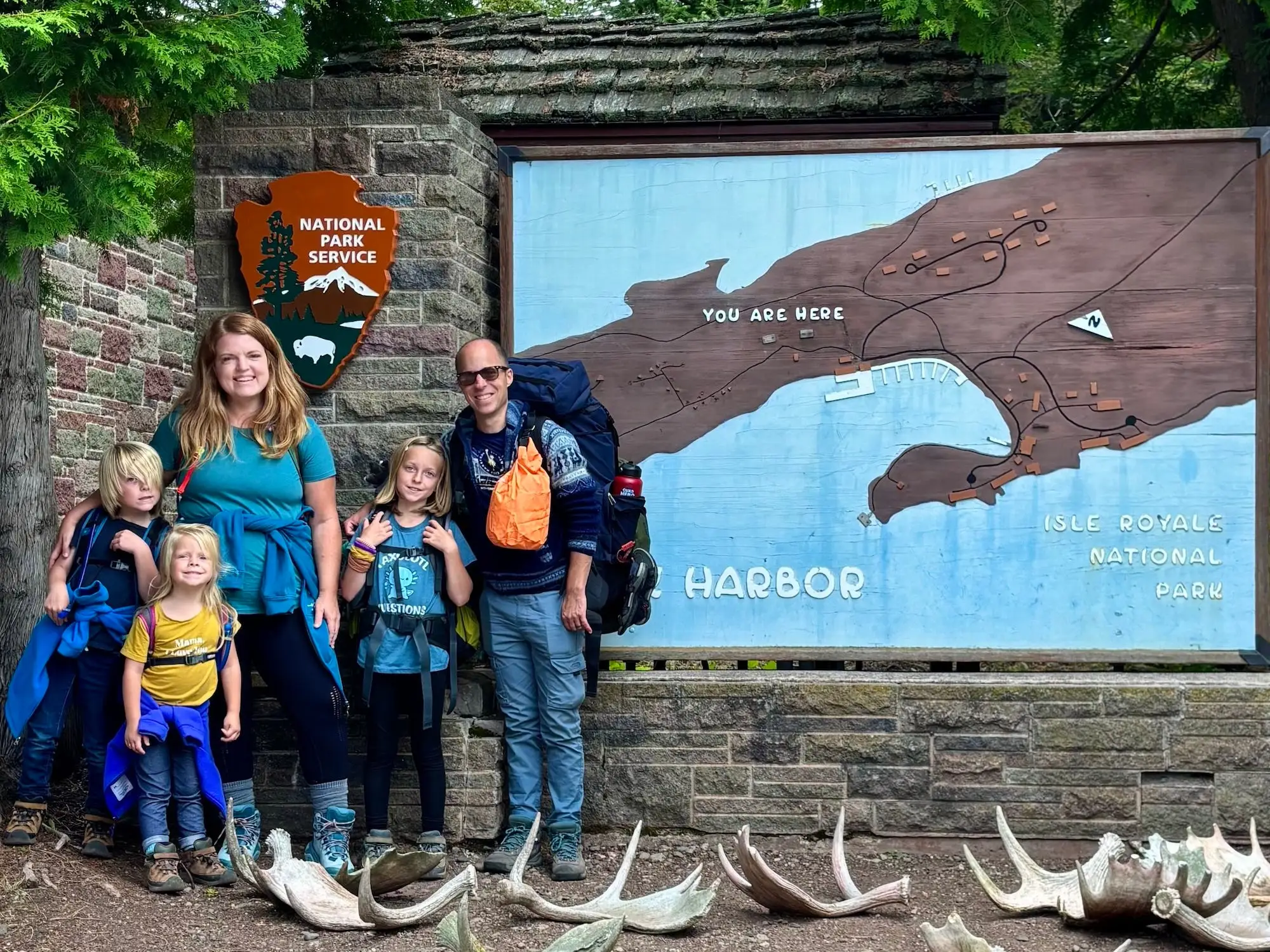 Five hikers with backpacks stand by the Isle Royale National Park harbor map and National Park Service sign.