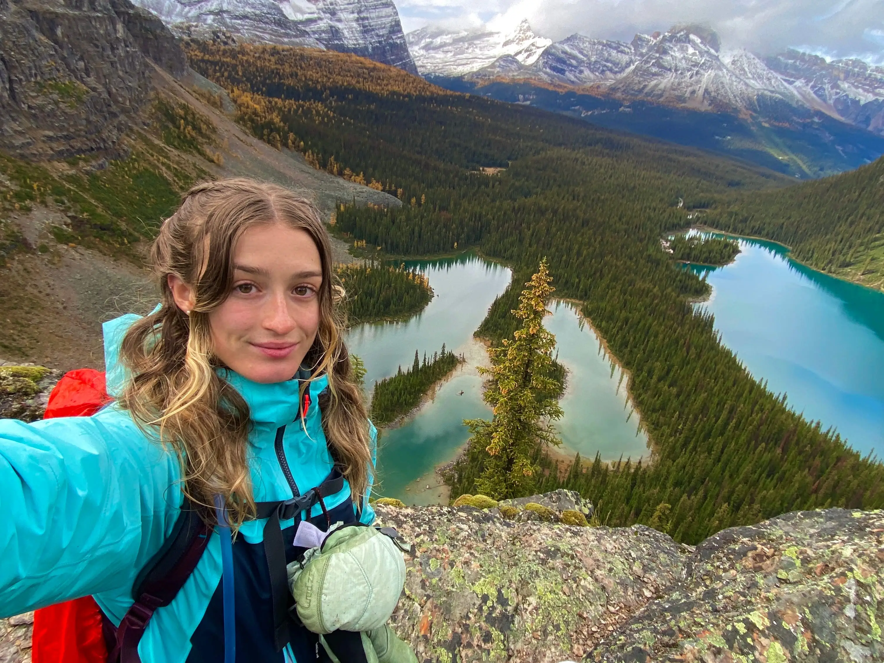 A woman takes a selfie on a mountain with two blue lakes in the background.