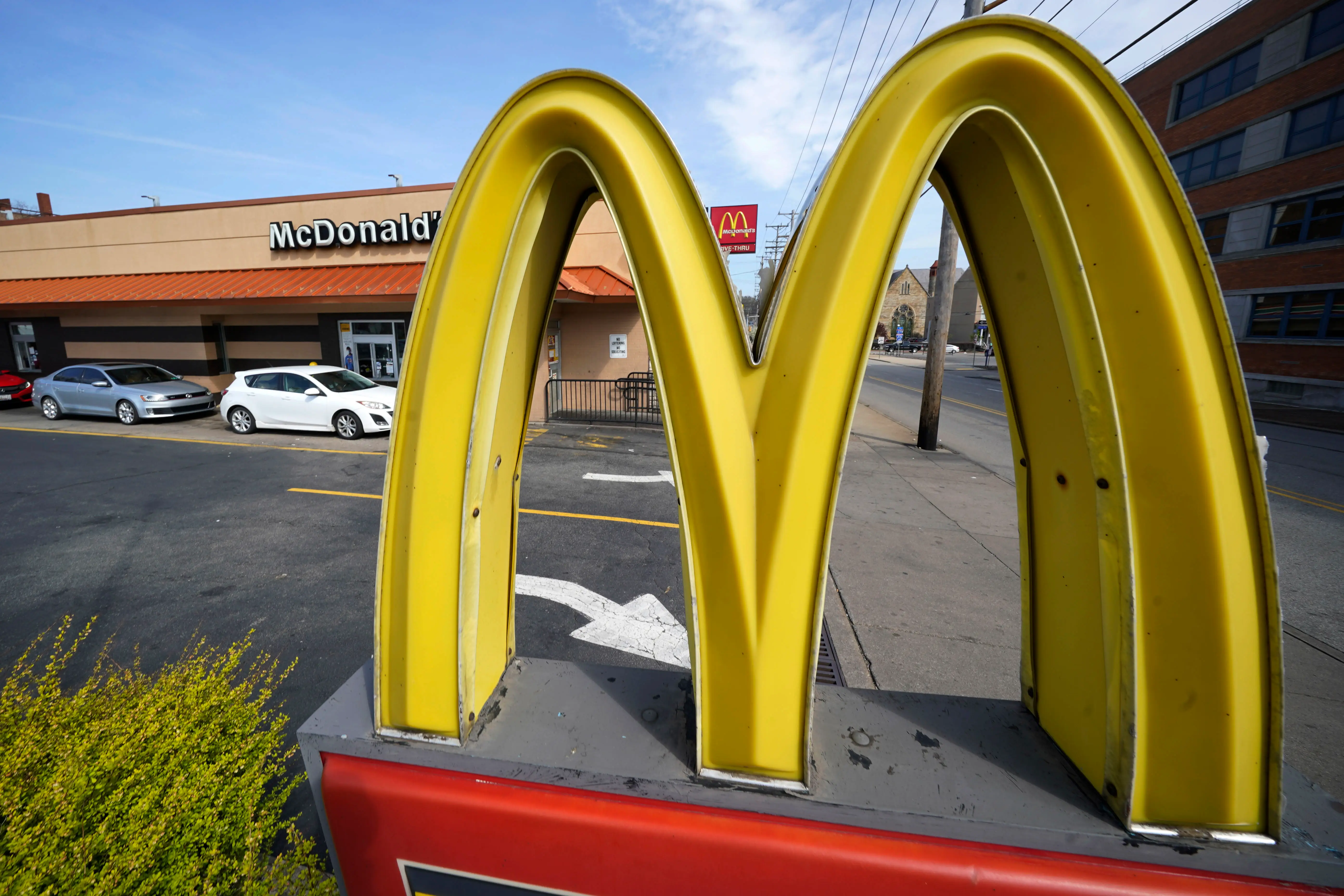 Large yellow McDonald's golden arches sign stands in front of a McDonald's restaurant and parking lot.