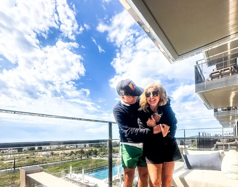 The writer's husband hugging her on a balcony, with a pool visible in the background.