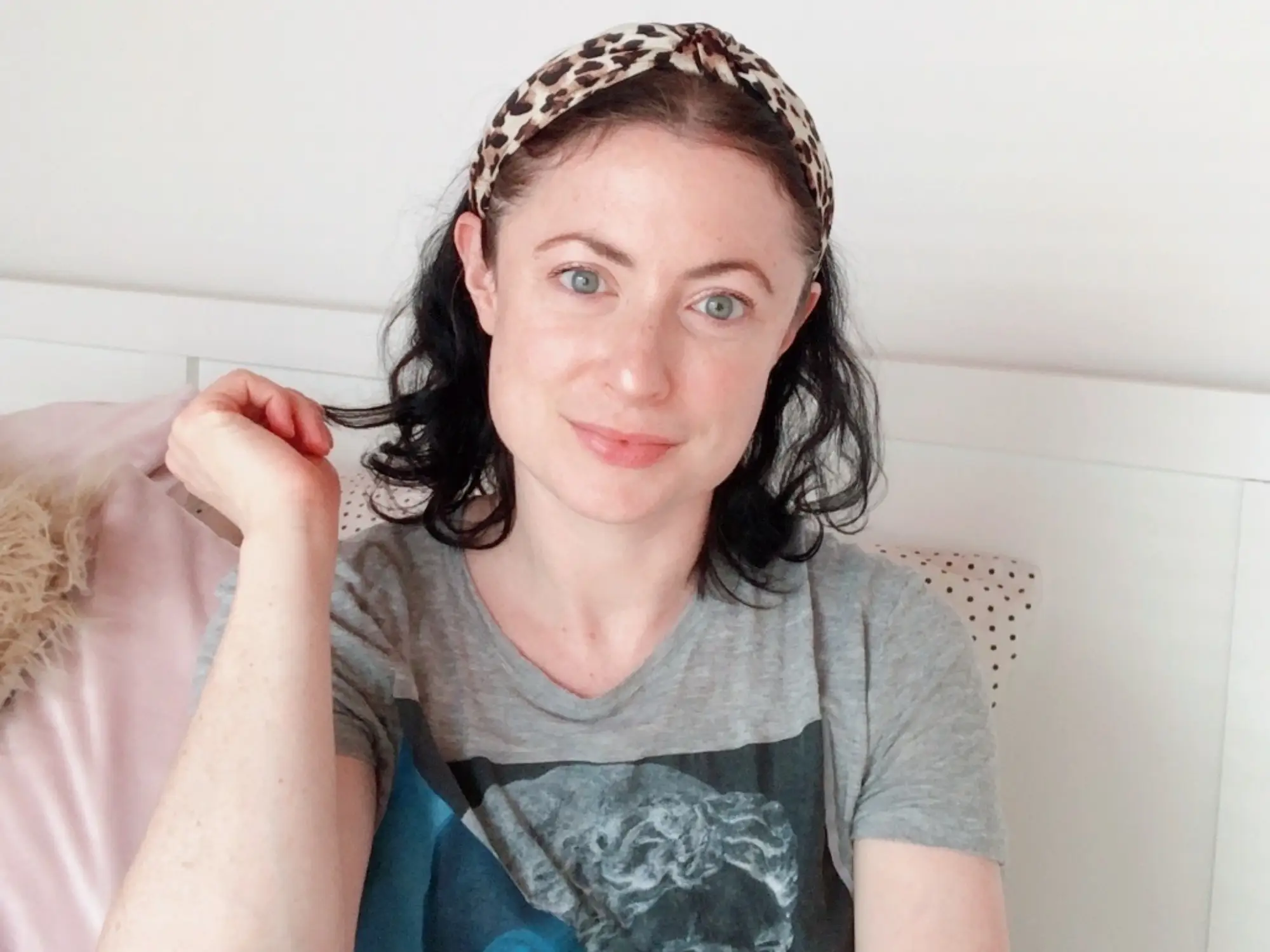 Woman in t-shirt, leopard print headband smiling, holding piece of hair