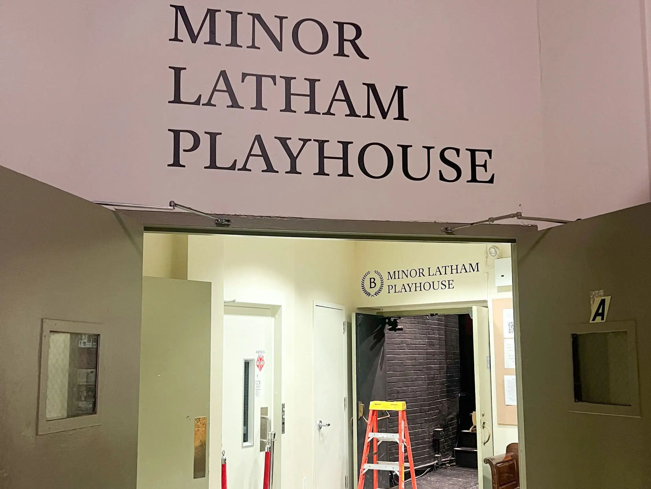 The entrance to Minor Latham Playhouse, with open doors, a checkered floor, a red ladder, and large wall signage.