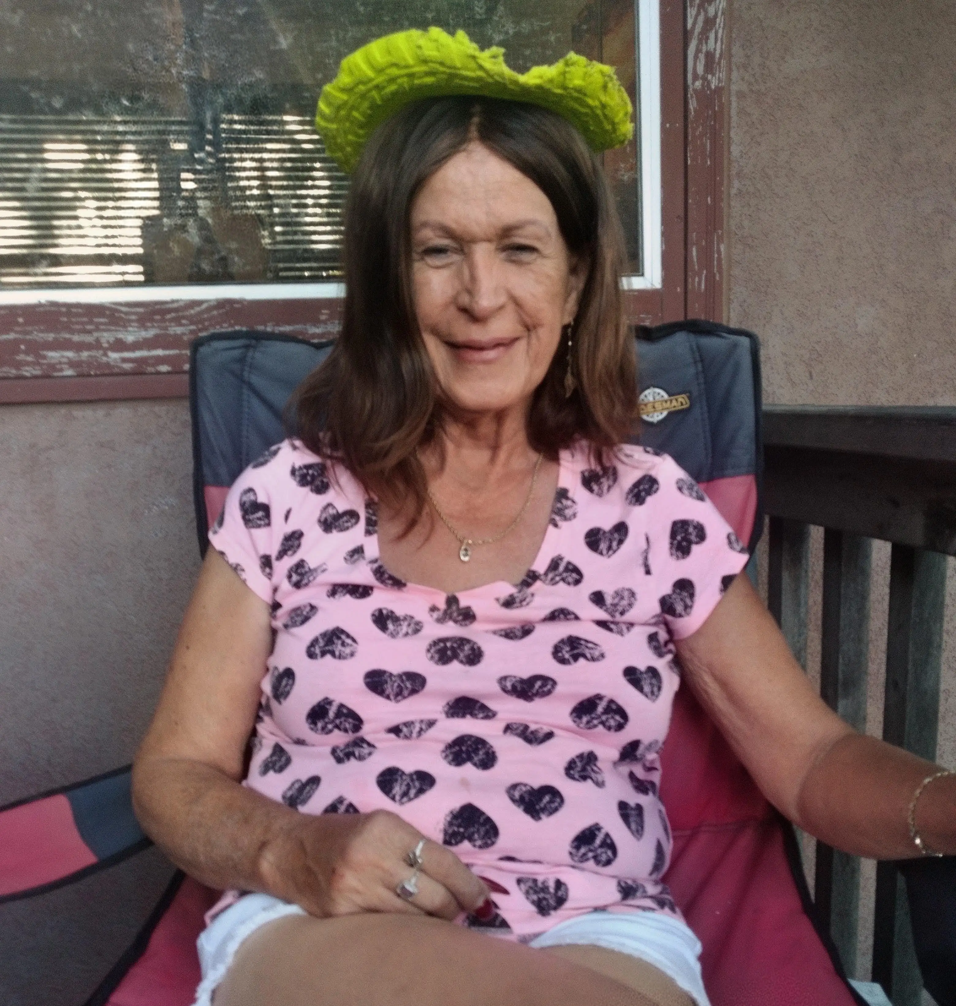 Person wearing a green knitted headband sits in a patio chair beside a window and railing.