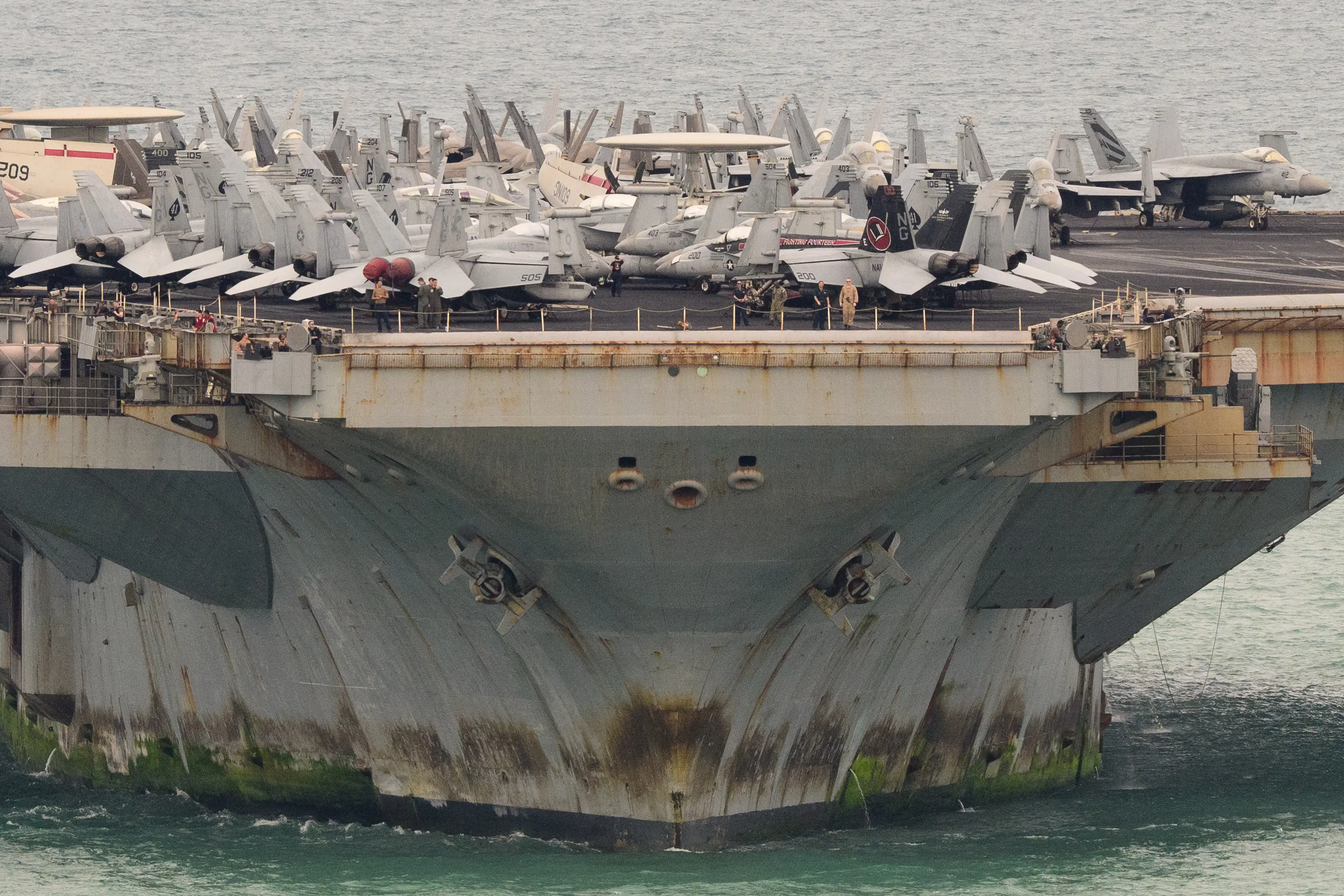 Military jets are parked tightly on the forward flight deck of an aircraft carrier at sea.
