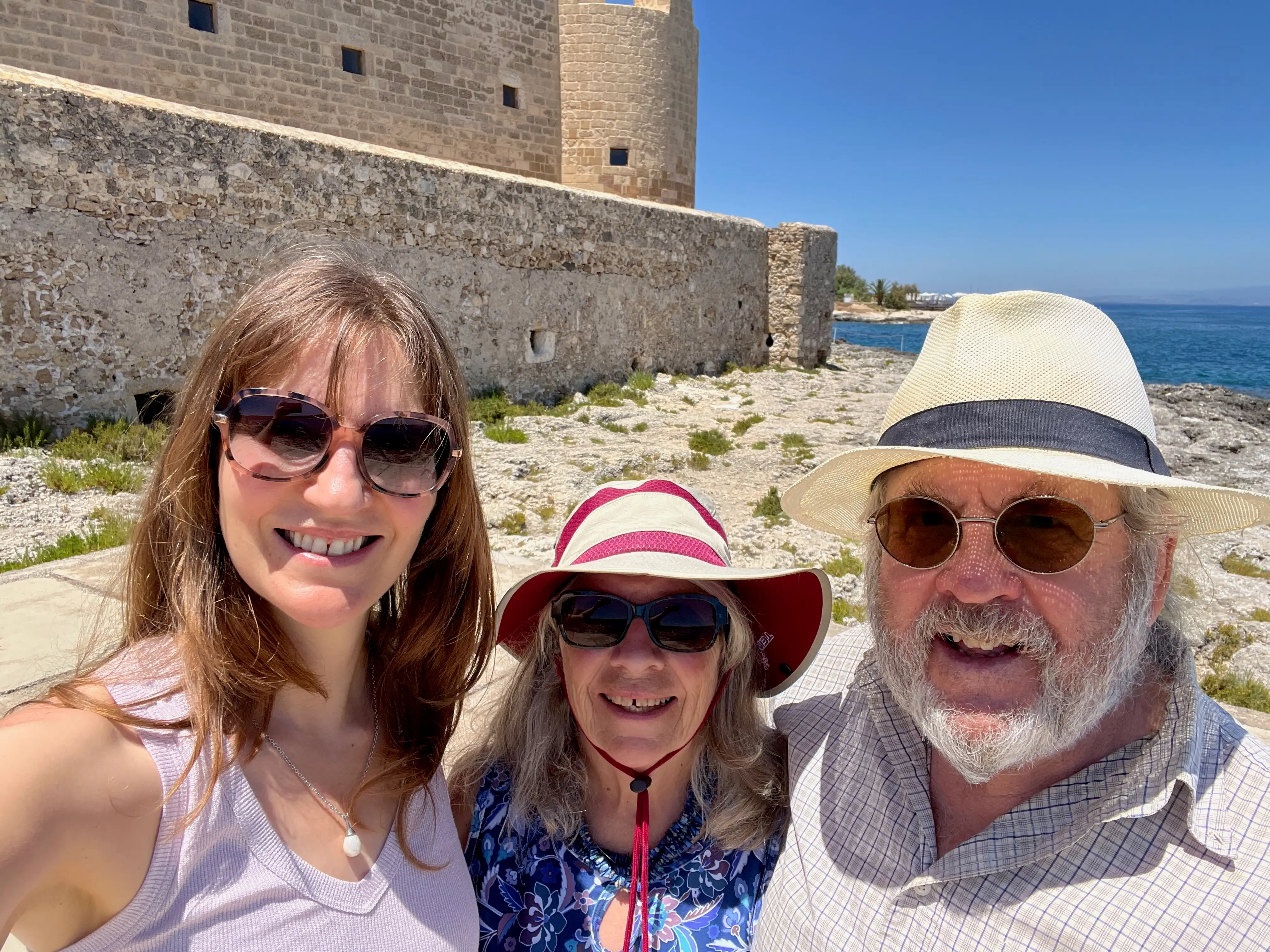 The author stands next to her two parents in Italy, with a body of water visible in the background.