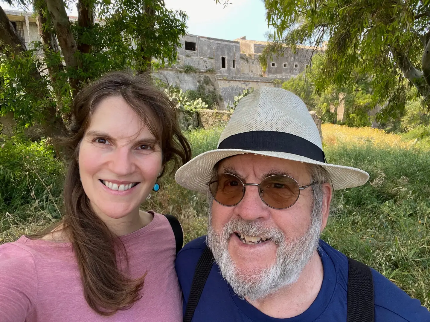 The writer smiling with her dad in Italy, with greenery and an old building in the background.