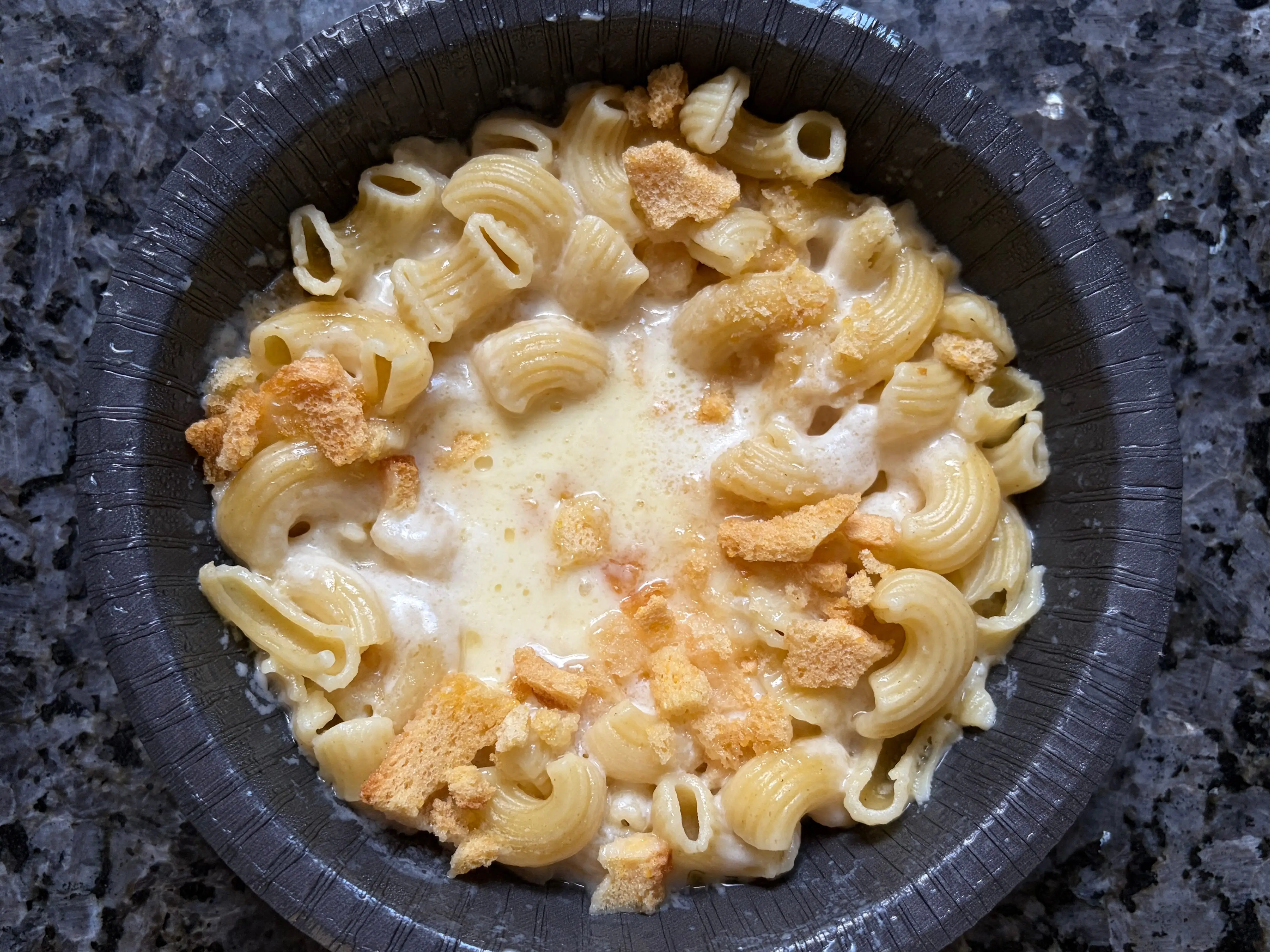 A microwavable bowl with elbow pasta, cheese sauce, and breadcrumbs.