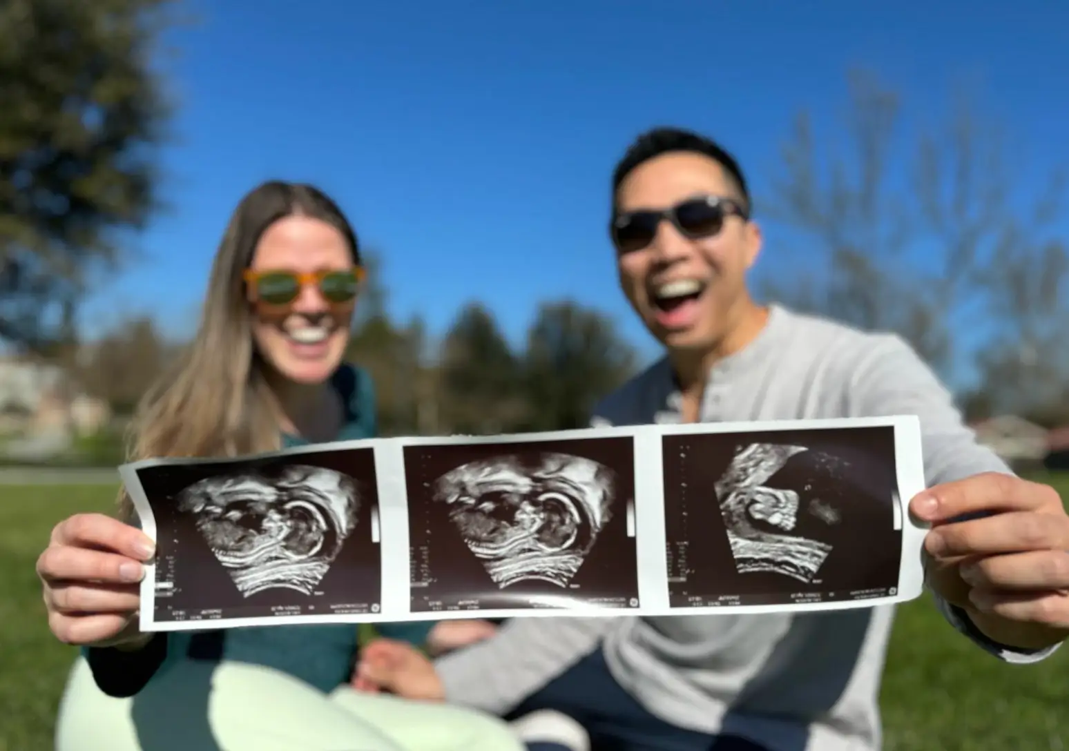 The writer and her husband sit outdoors, holding a strip of three black-and-white ultrasound images toward the camera.