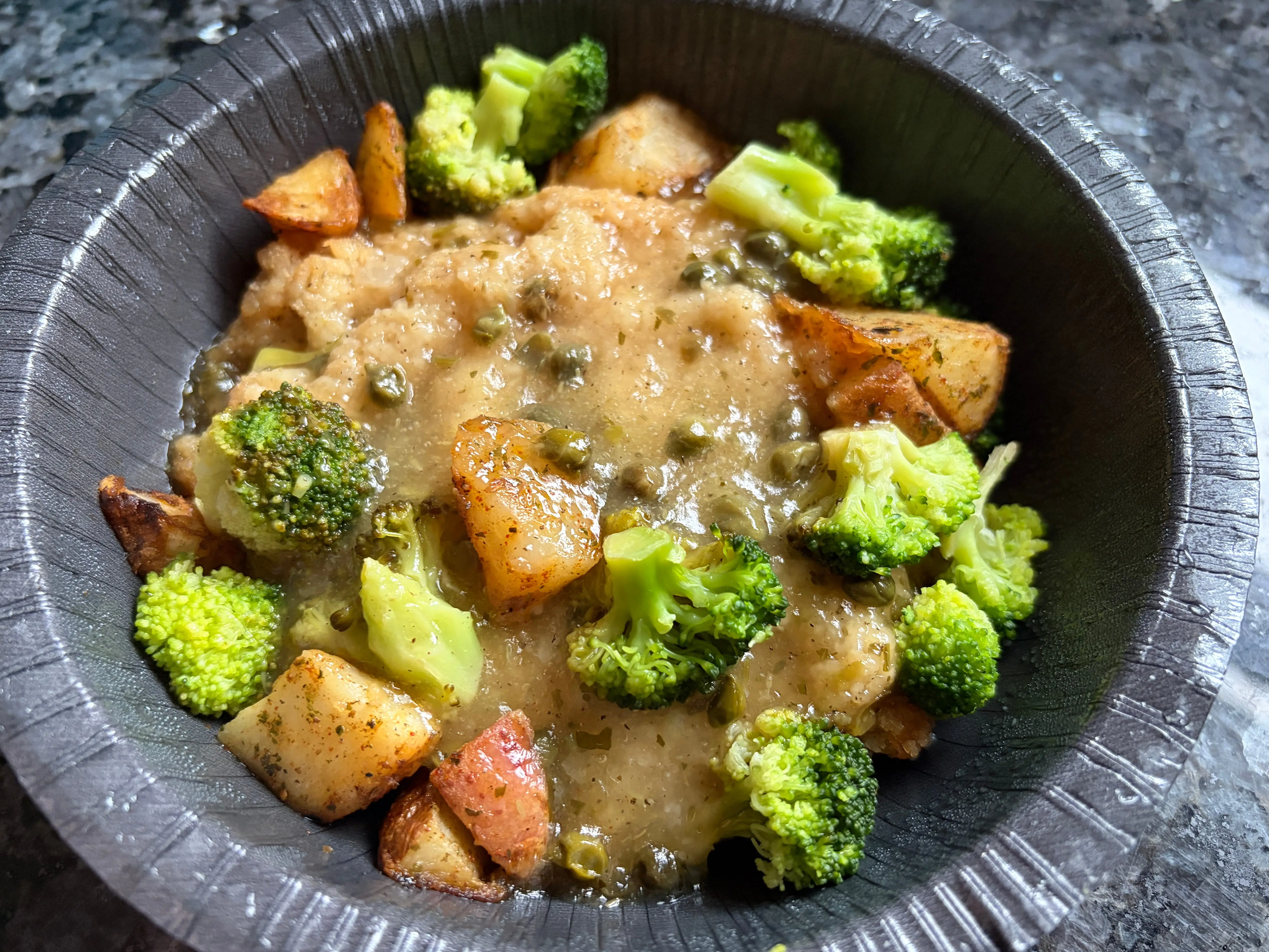 Breaded chicken in a bowl with broccoli, potatoes, capers, and sauce.