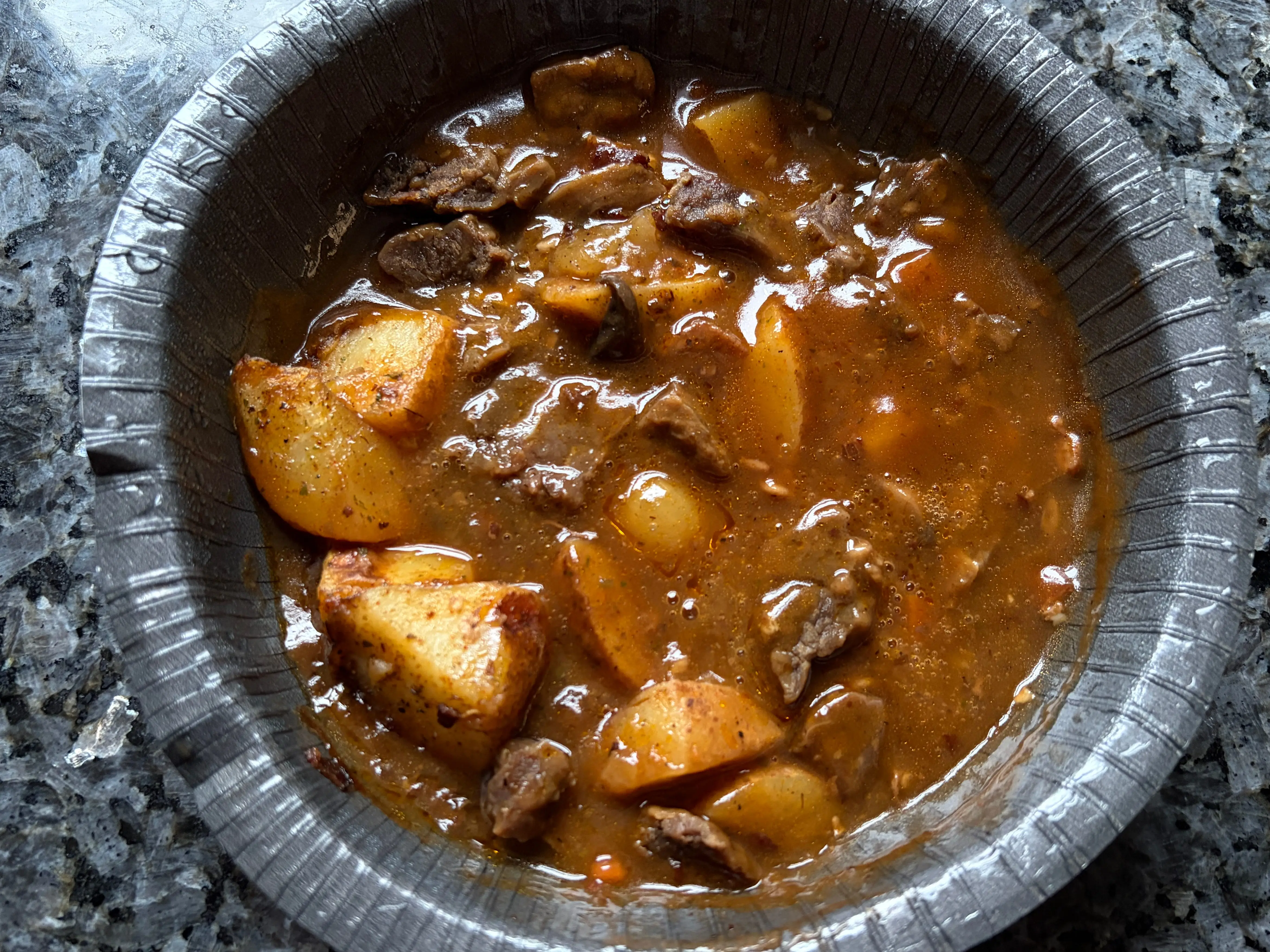 Pieces of beef in a bowl with brown sauce, potatoes, and onions.