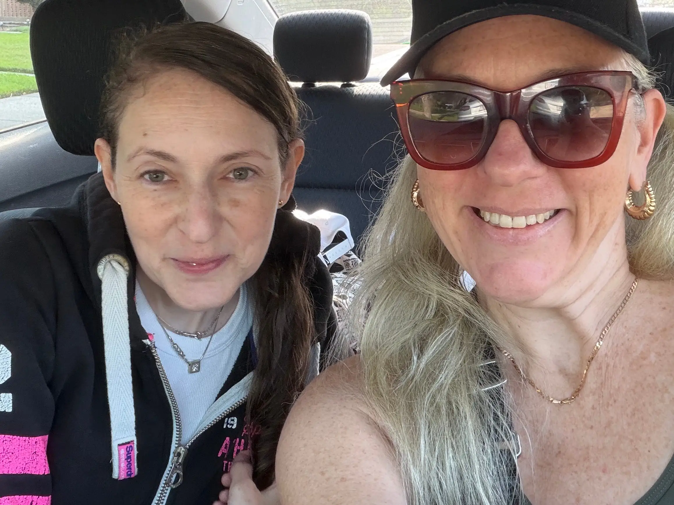 Two people sit closely together in the back seat of a car, with one wearing sunglasses and a black cap.
