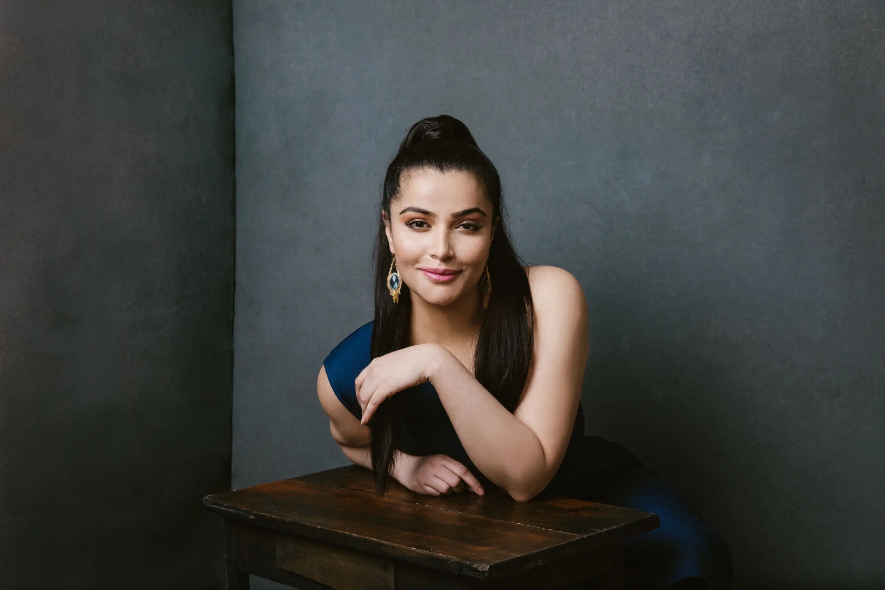 sameera sulliven leaning on a wooden table smiling at the camera