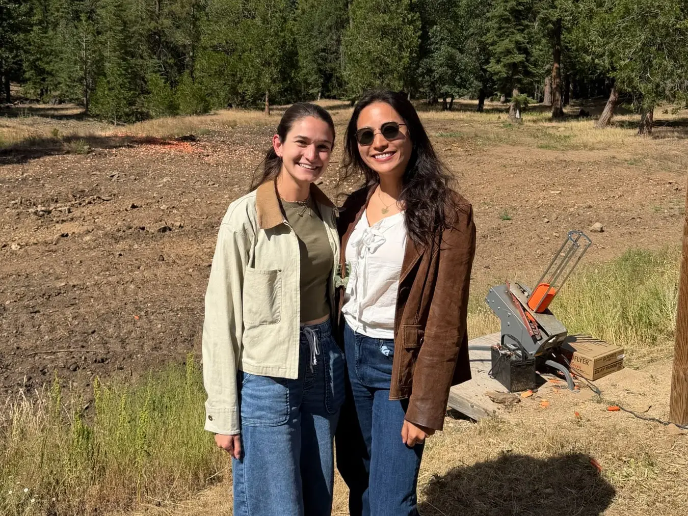 Anna and her friend Ellie pose for a photo in a grassy area surrounded by trees.