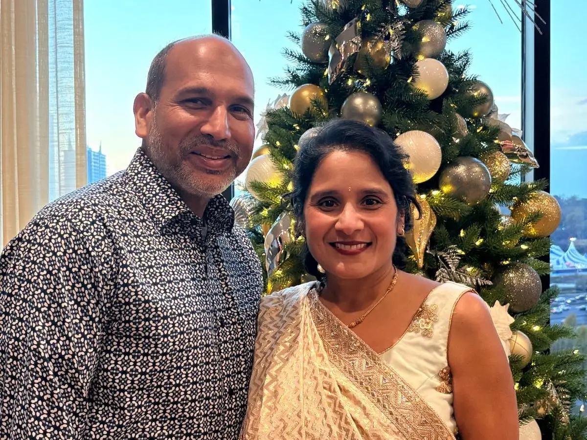 Dr. Munjal Shroff  and his iwfe pose beside a decorated Christmas tree in front of large windows with a city view.