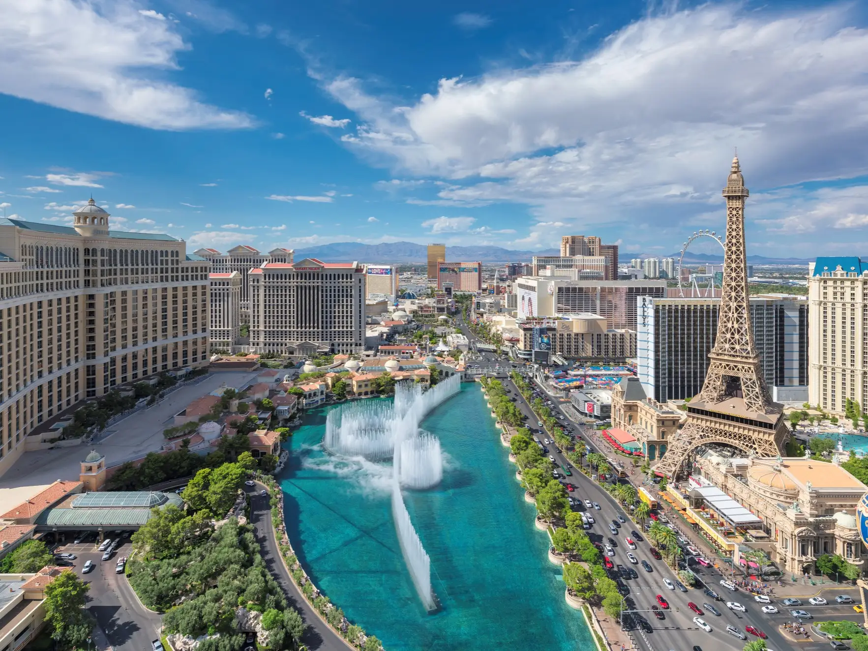 Las Vegas Strip skyline with Bellagio fountains and the Paris Las Vegas Eiffel Tower under a partly cloudy sky.
