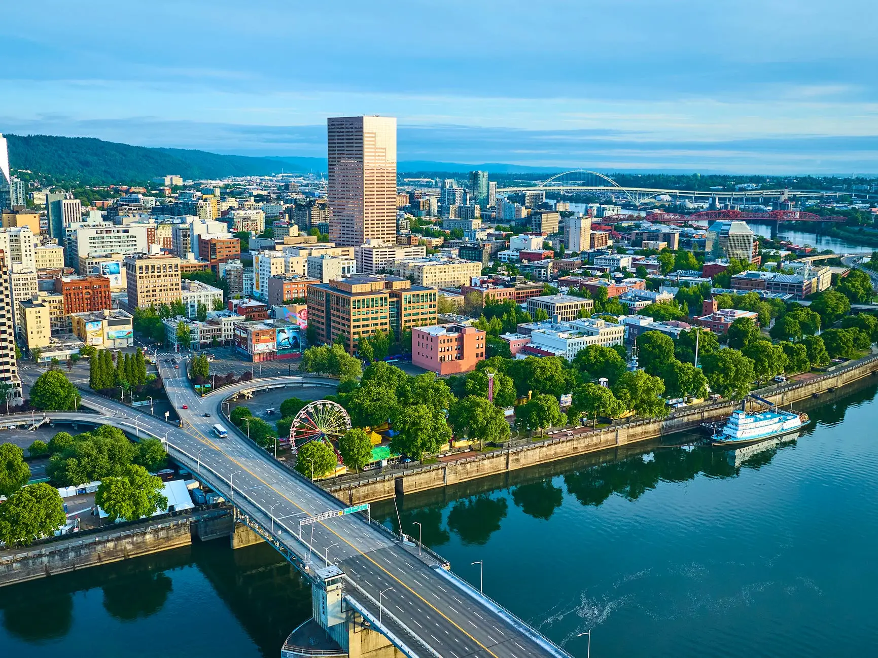 Downtown Portland skyline rises beside the Willamette River with bridges, waterfront trees, and a ferris wheel.