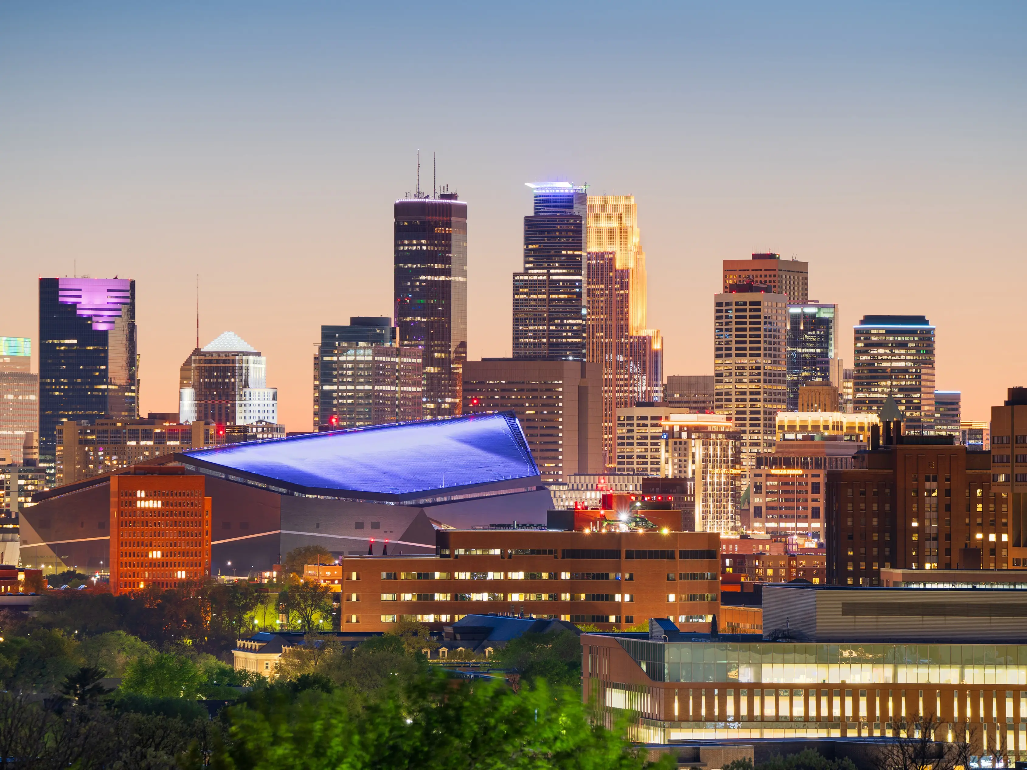 Downtown Minneapolis skyline at dusk with U.S. Bank Stadium illuminated beneath tall office towers.