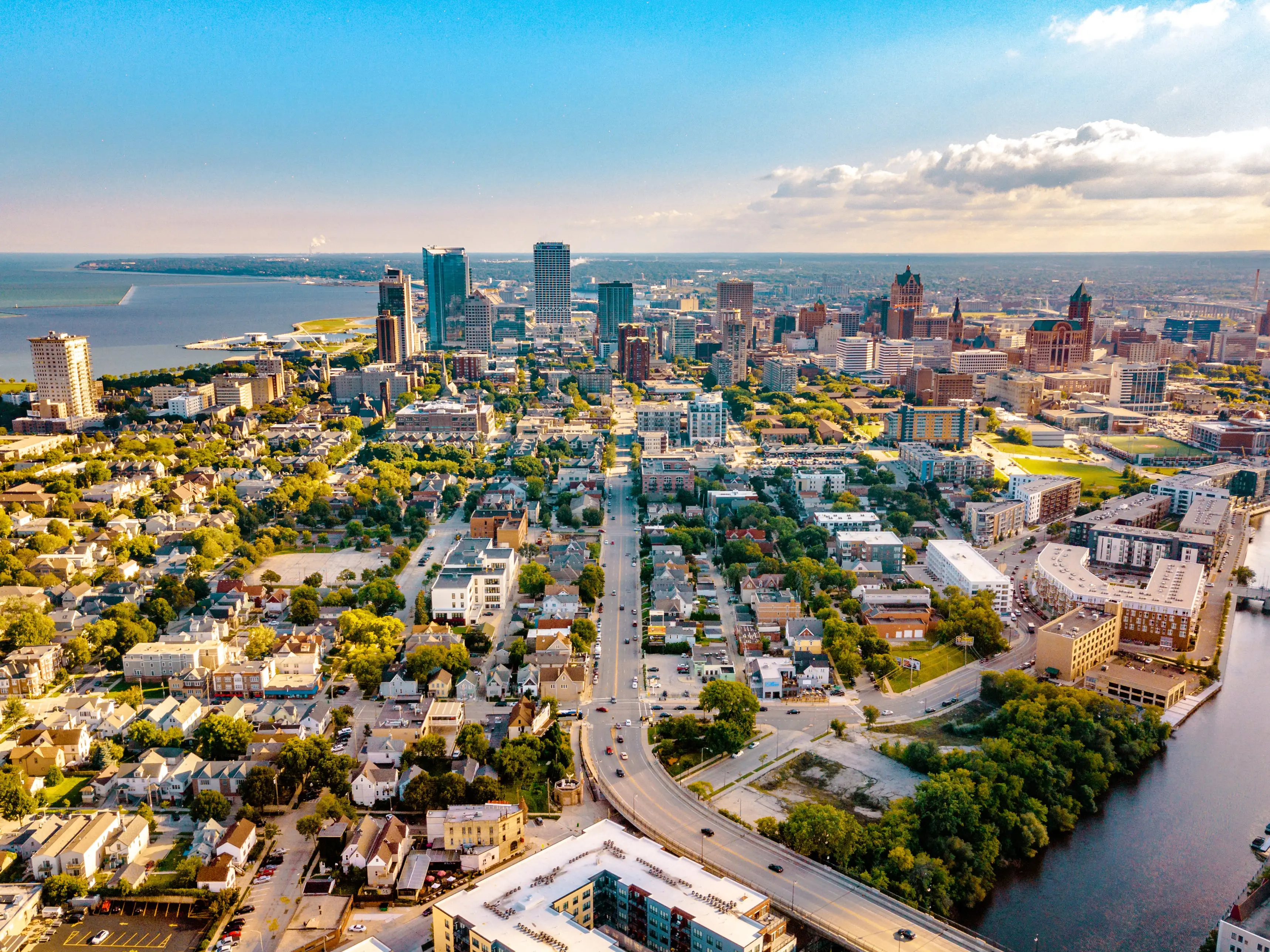 Aerial view of downtown Milwaukee skyline with surrounding neighborhoods, Lake Michigan, and the Milwaukee River at sunset.