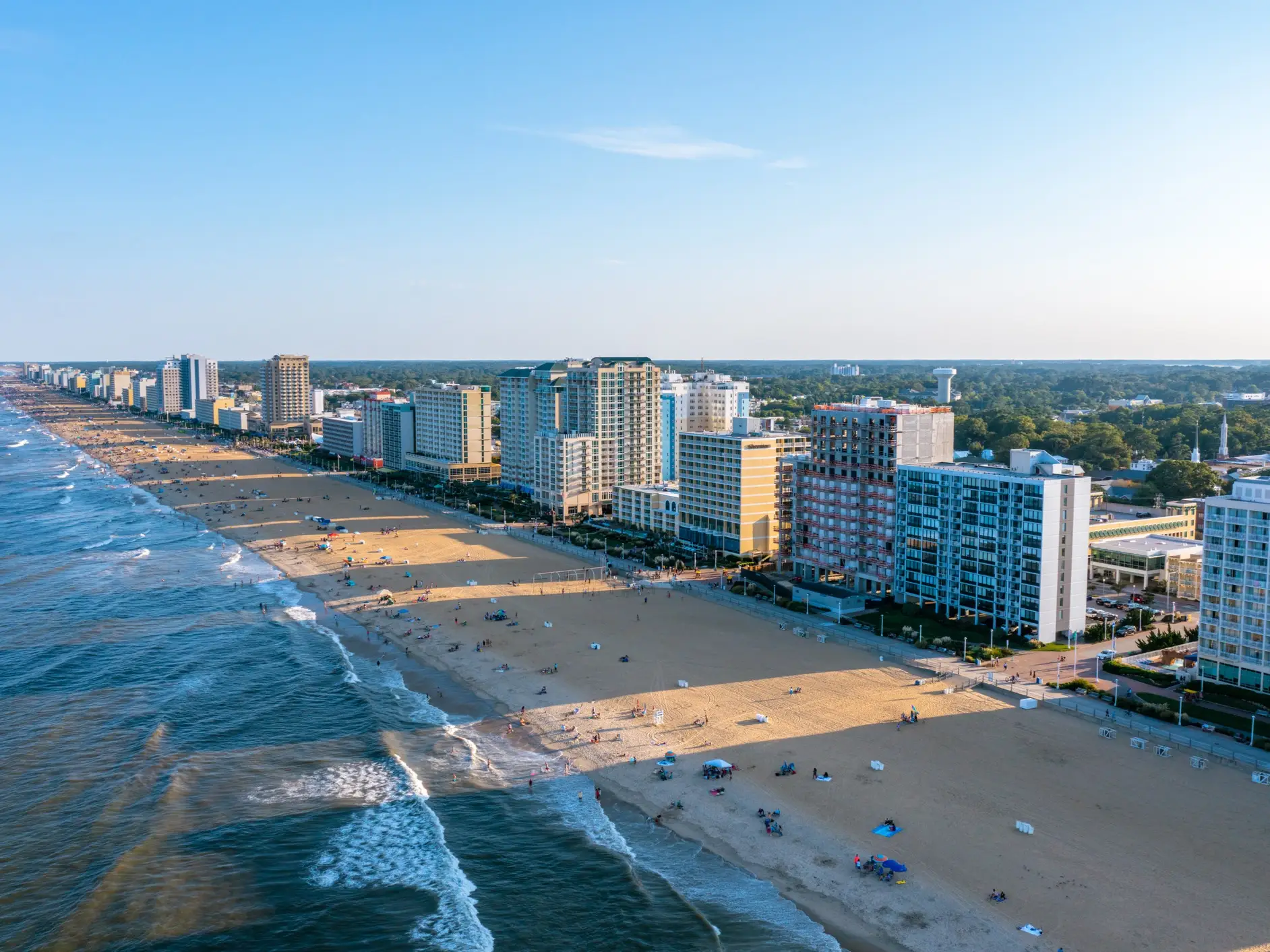 Aerial view of a wide sandy beach lined with high-rise oceanfront buildings beside waves under a clear sky.