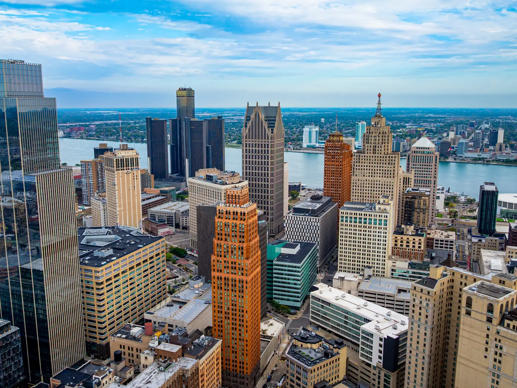 Downtown Detroit skyline with the Detroit River and high-rise buildings under a partly cloudy sky.