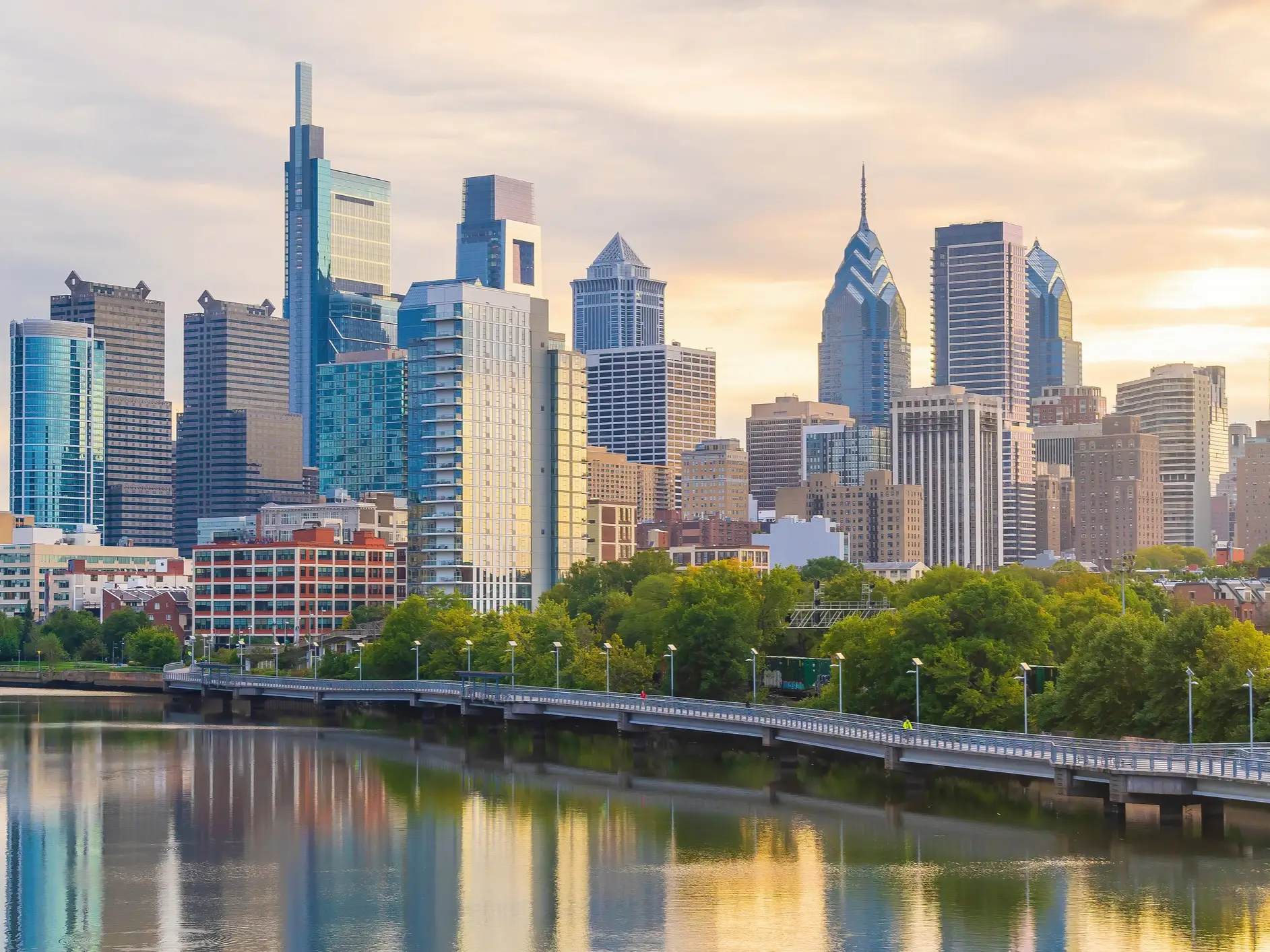 Center City Philadelphia skyline rises above the Schuylkill River with bridge traffic and sunset reflections.