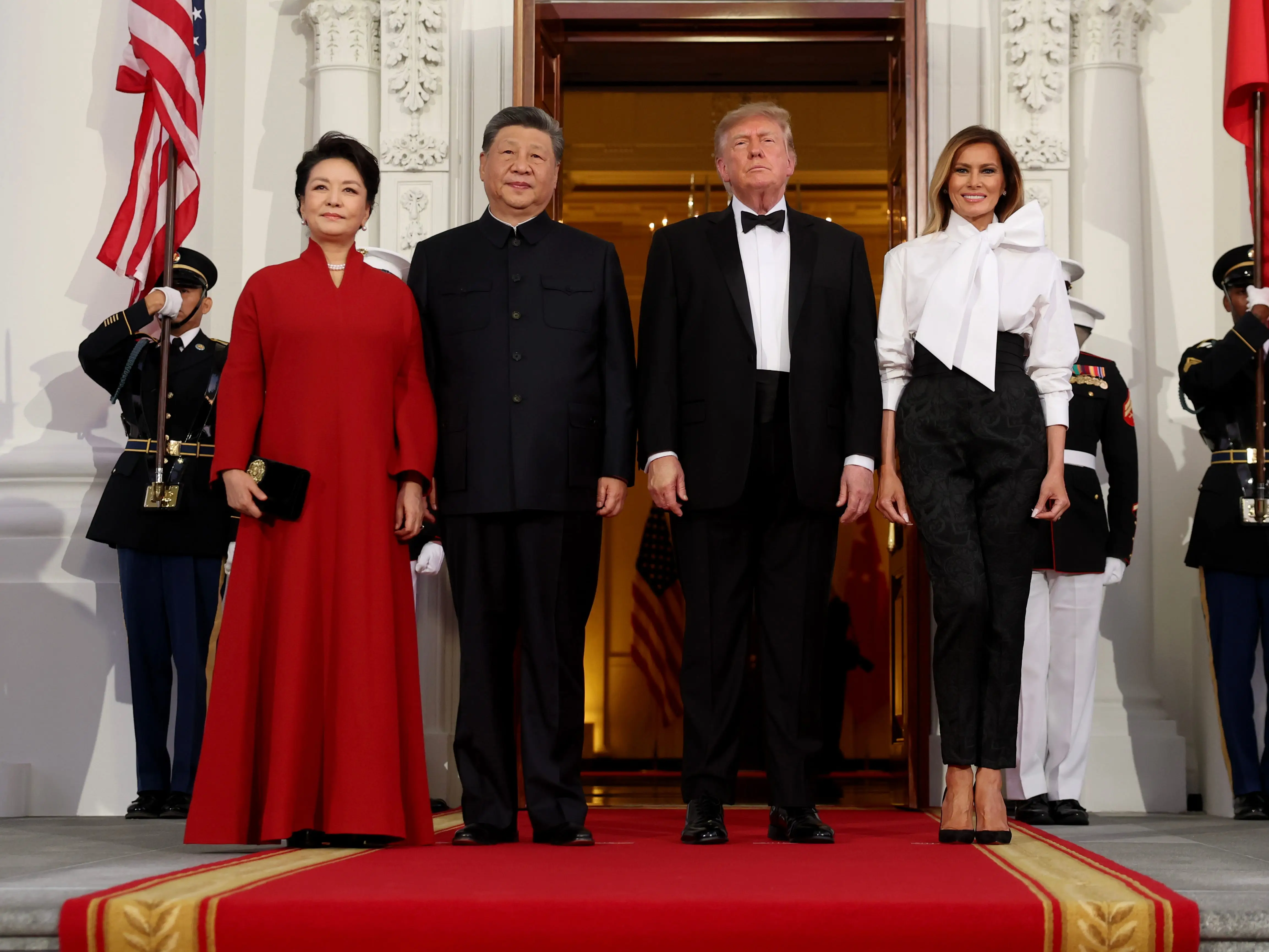 Xi Jinping, Peng Liyuan, Donald Trump and Melania Trump stand on a red carpet between U.S. and Chinese flags.