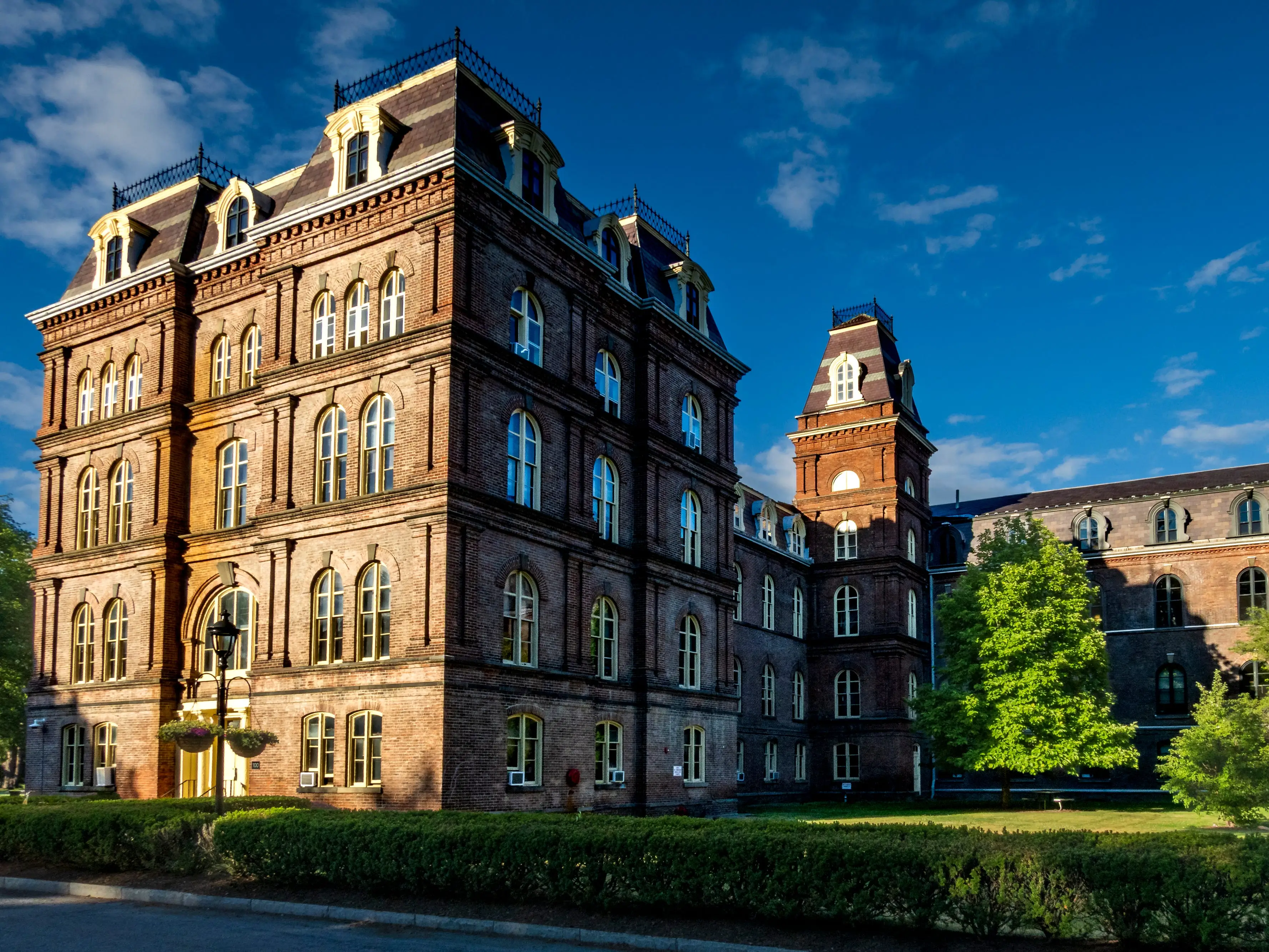 Poughkeepsie, NY - US - Jun 15, 2026 Sunlit view of Vassar College featuring historic red-brick architecture, mansard roofs, and lush green grounds under a vivid blue summer sky.