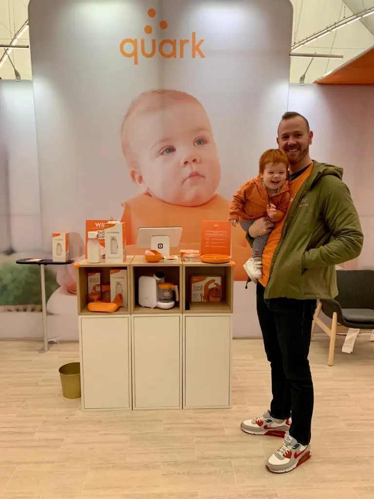 Garett Senez is pictured with his kid in front of a Quark Baby sign.