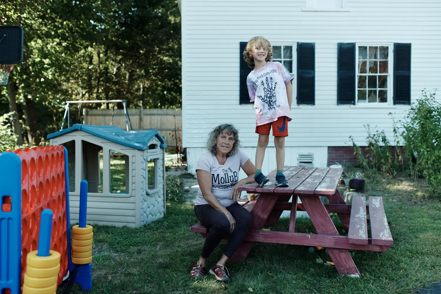A woman is sitting at a picnic table, with her son standing on top of it.