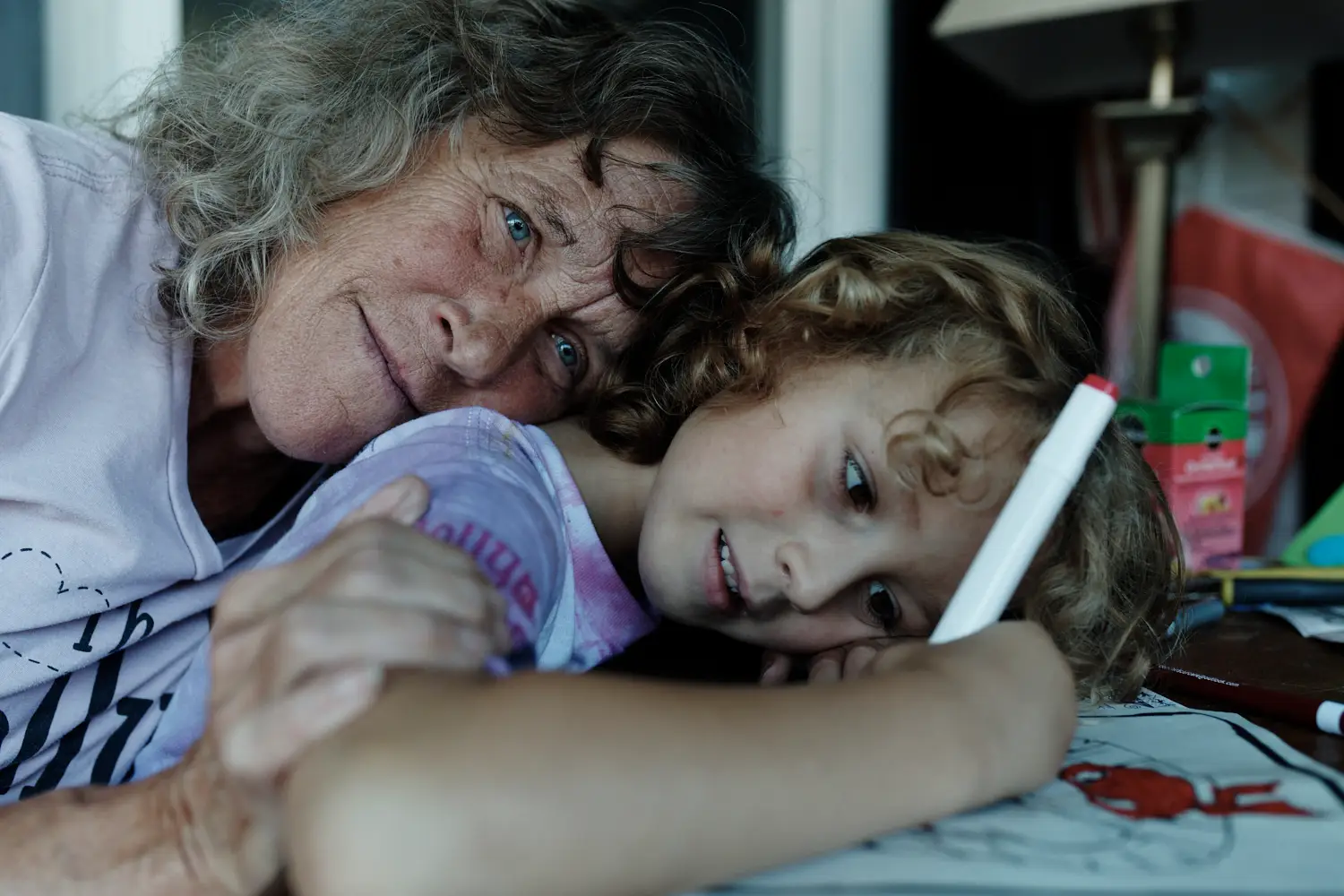 A mom cradles her young son as he colors with a red pen.
