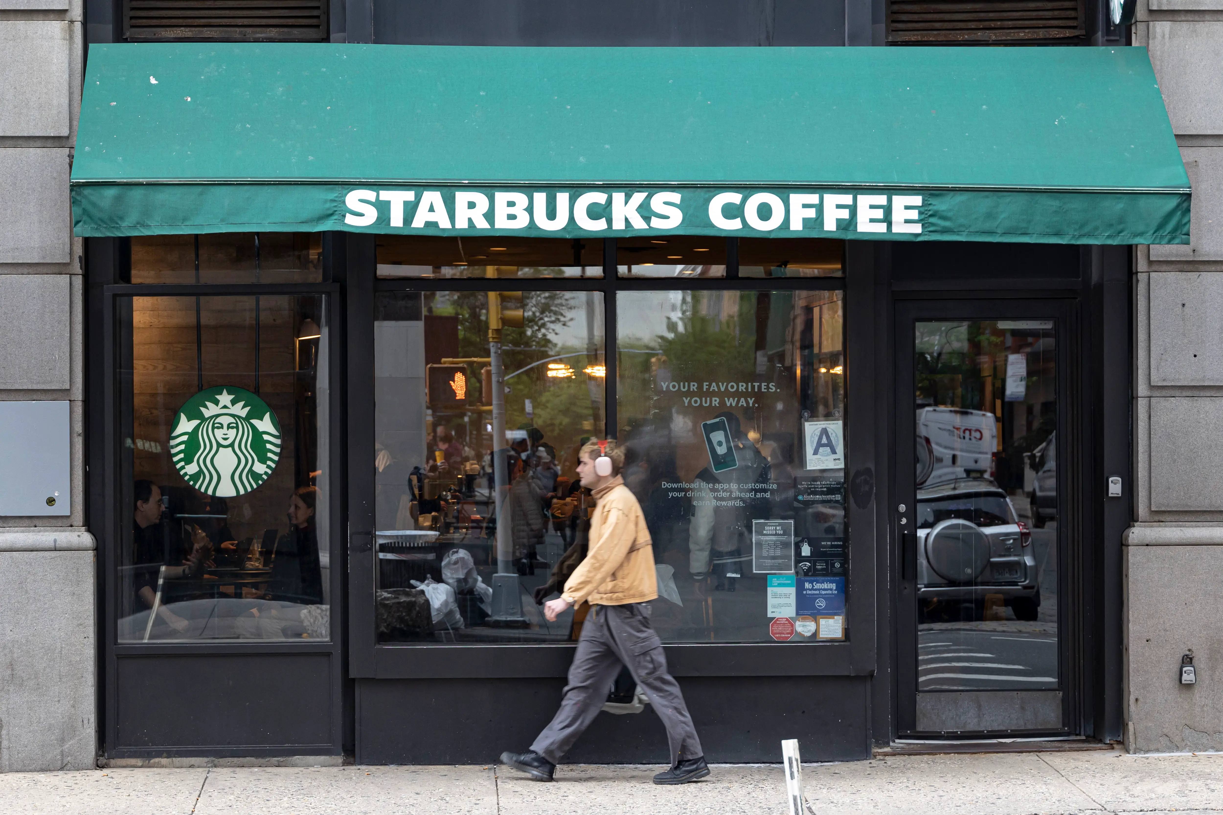 Starbucks Coffee storefront with a green awning and a pedestrian walking past the entrance.