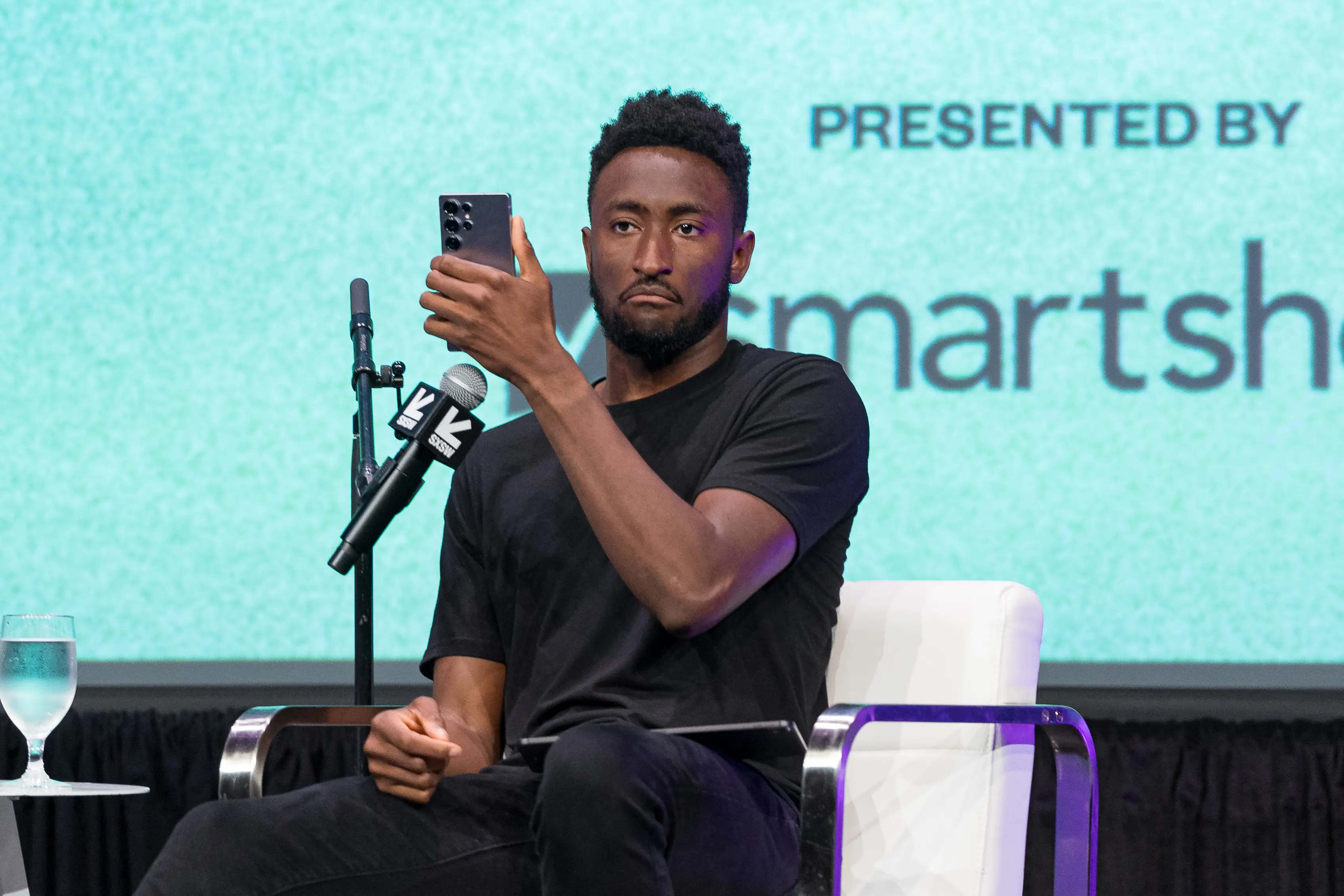YouTuber Marques Brownlee holds a phone in his left hand during an onstage interview.