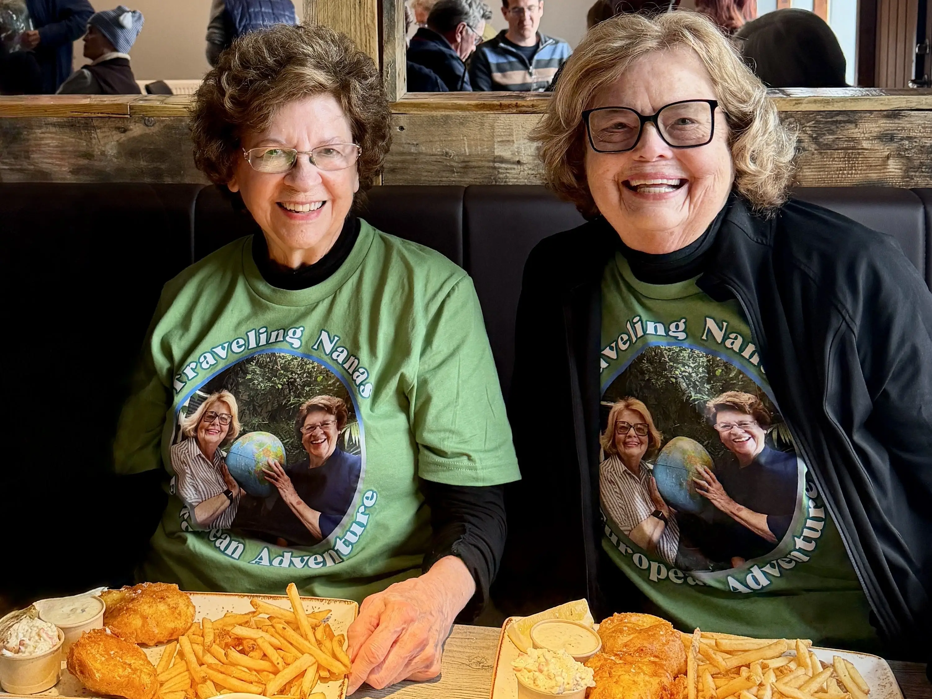 The writers, in their matching T-shirts, sit at a restaurant table in Iceland, with two plates of fish and chips.