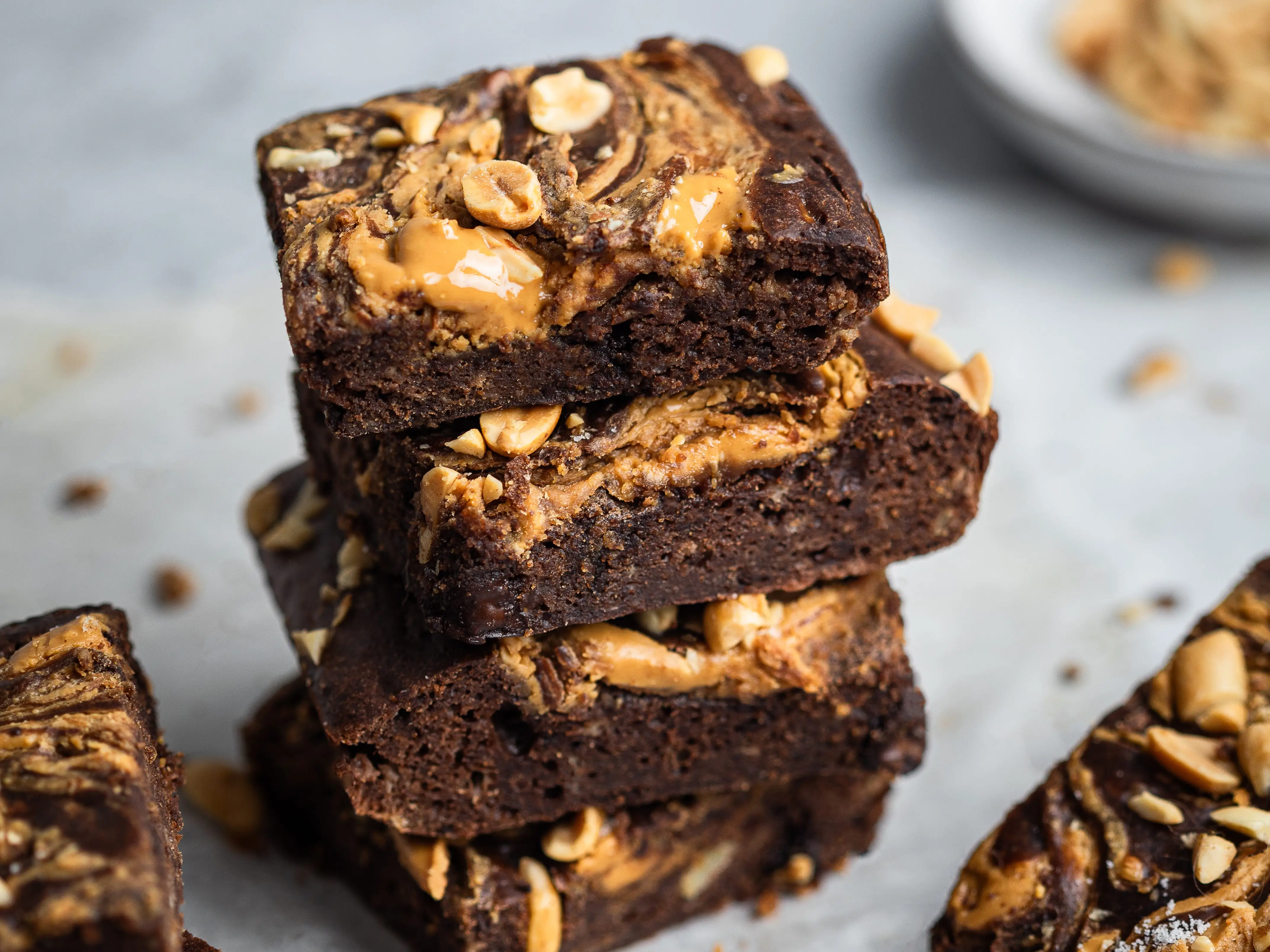 Stacked chocolate brownies with peanut butter swirls and chopped peanuts on parchment paper.