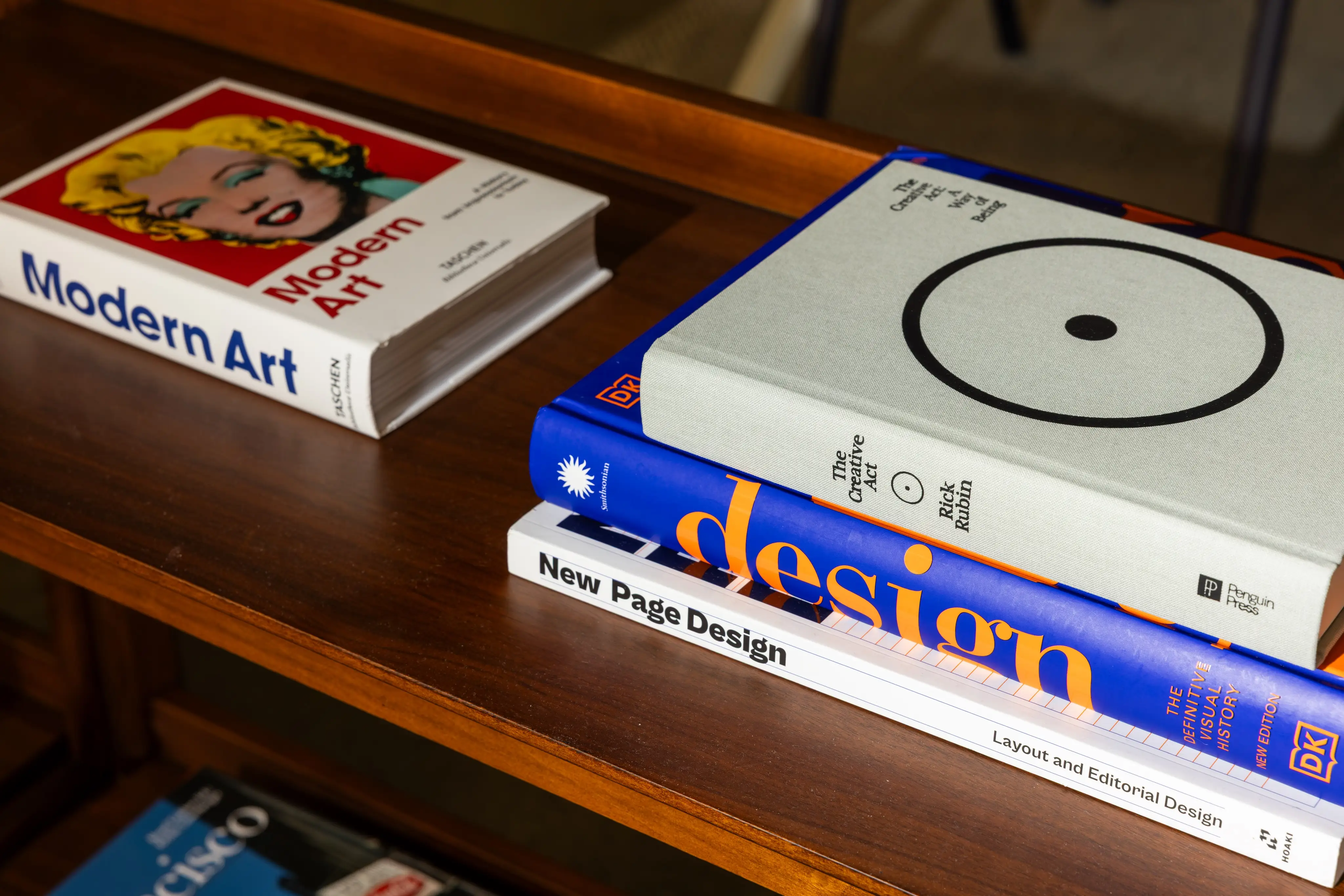 Art and graphic design books are arranged on a polished wooden shelf.