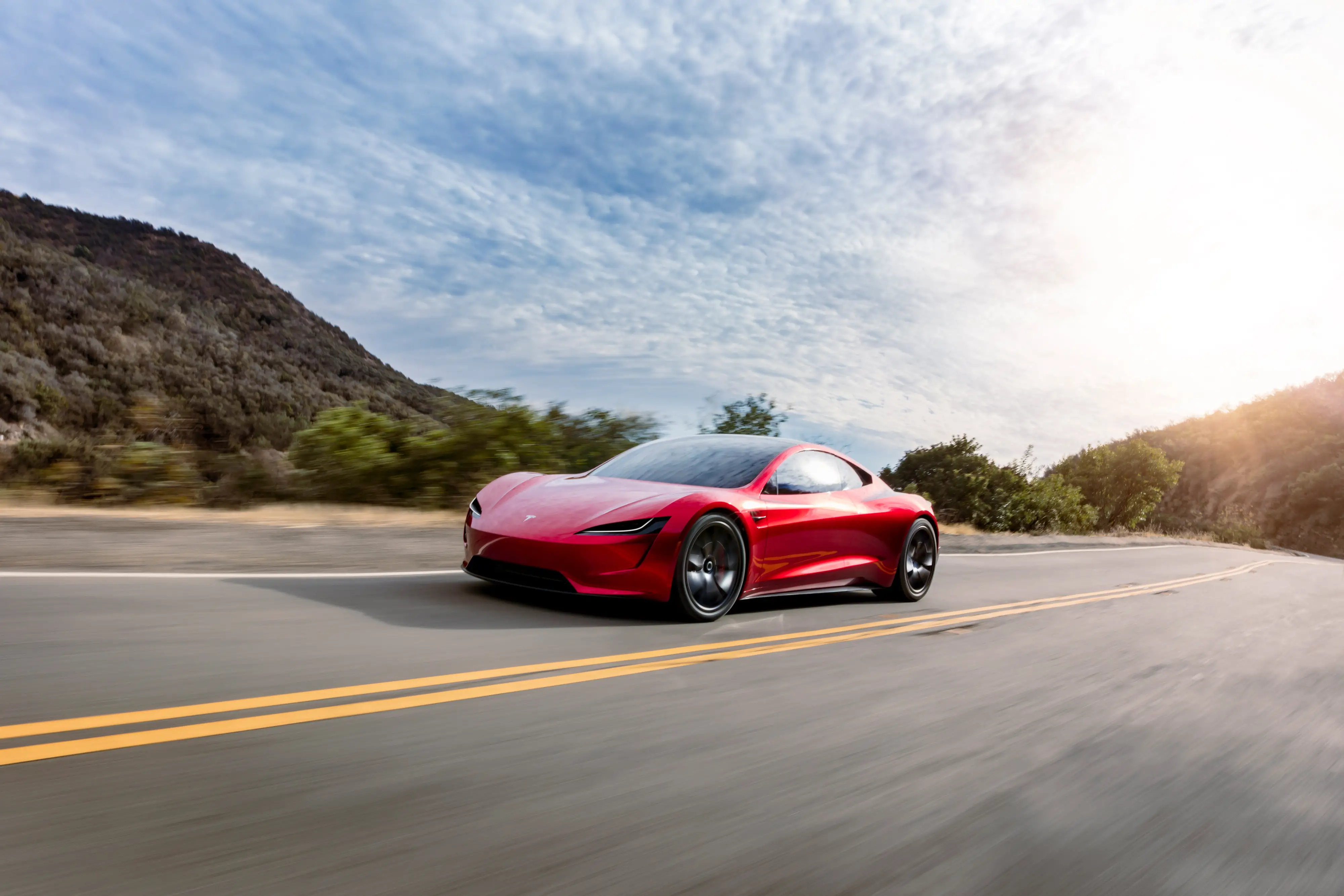 A red Tesla Roadster prototype drives down a two-lane road.