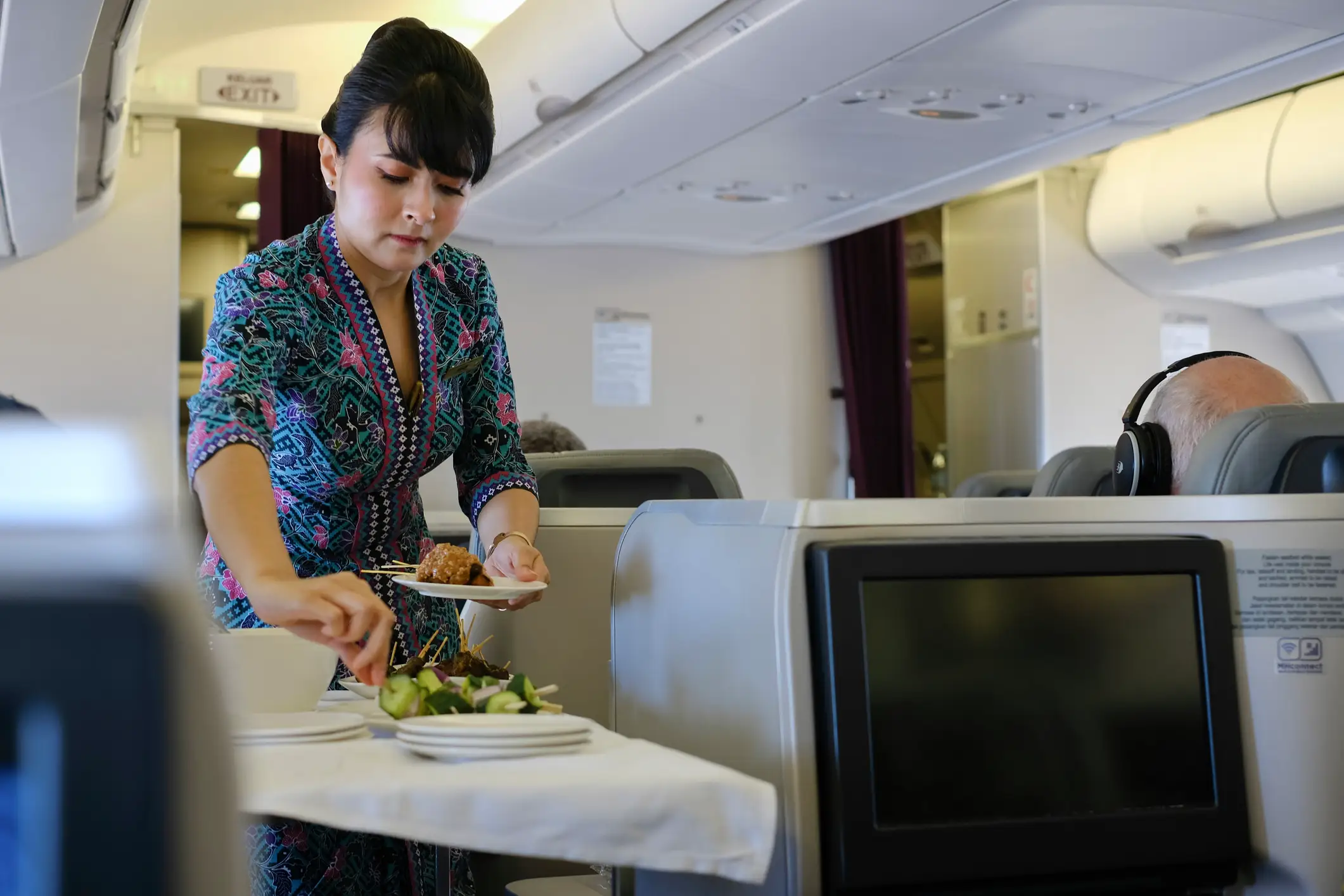 Kuala Lumpur, Malaysia - Oct 17, 2023: a Malaysian Airlines flight attendant serves an appetizer of chicken and beef sate skewers as part of an in-flight meal to a passenger on a Malaysia Airlines business class flight from Sydney to Kuala Lumpur