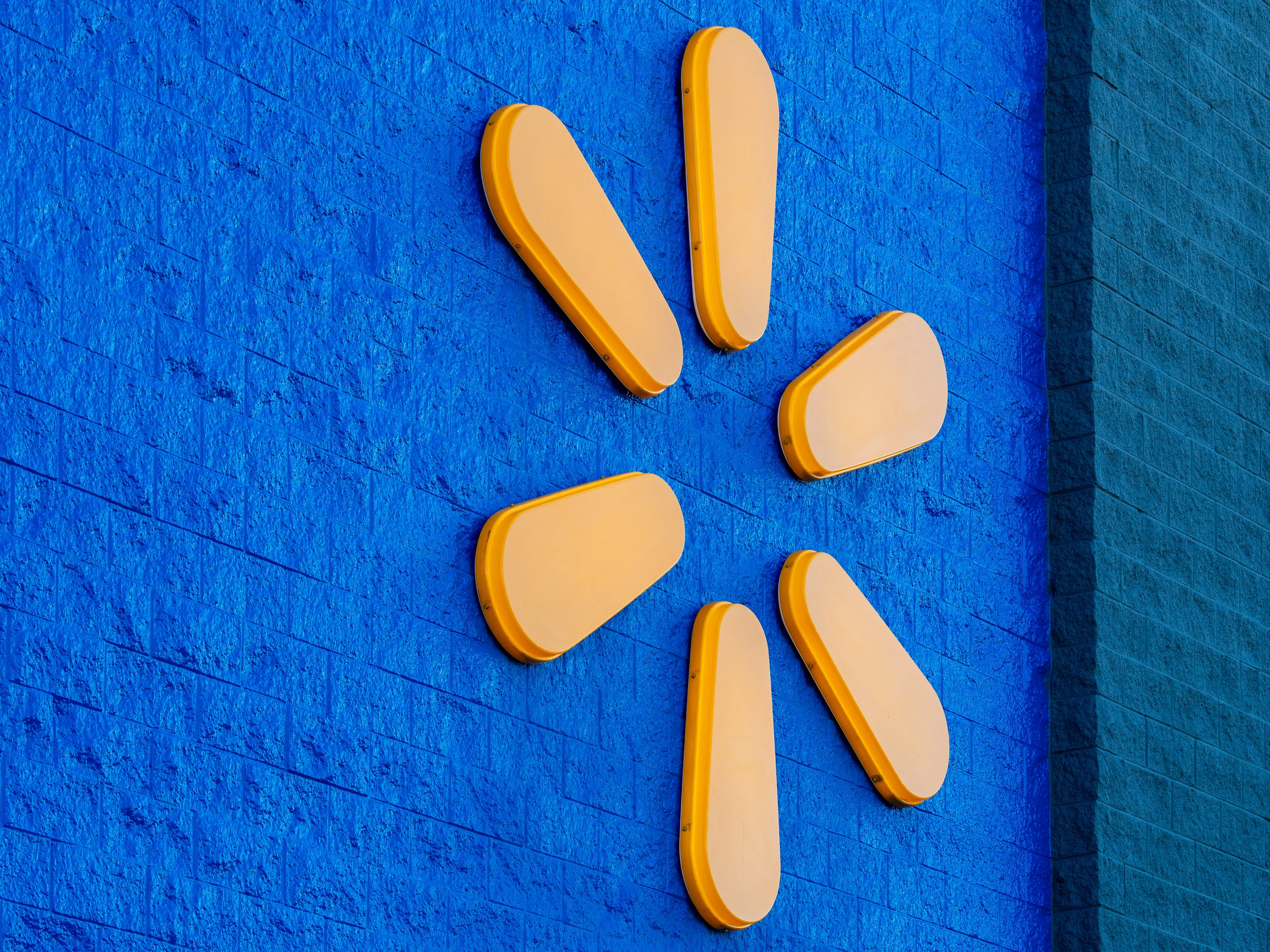 A close-up view shows the yellow Spark logo icon mounted on the blue brick exterior facade of a Walmart retail store in American Fork, Utah.