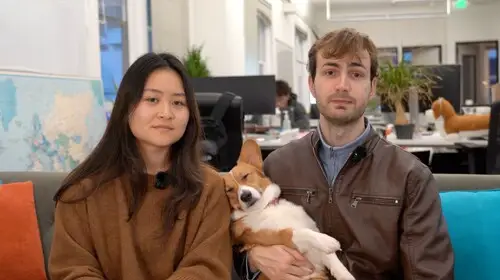 Emily Yuan and Nico Laqua sit in an office lounge while holding a Corgi between them.