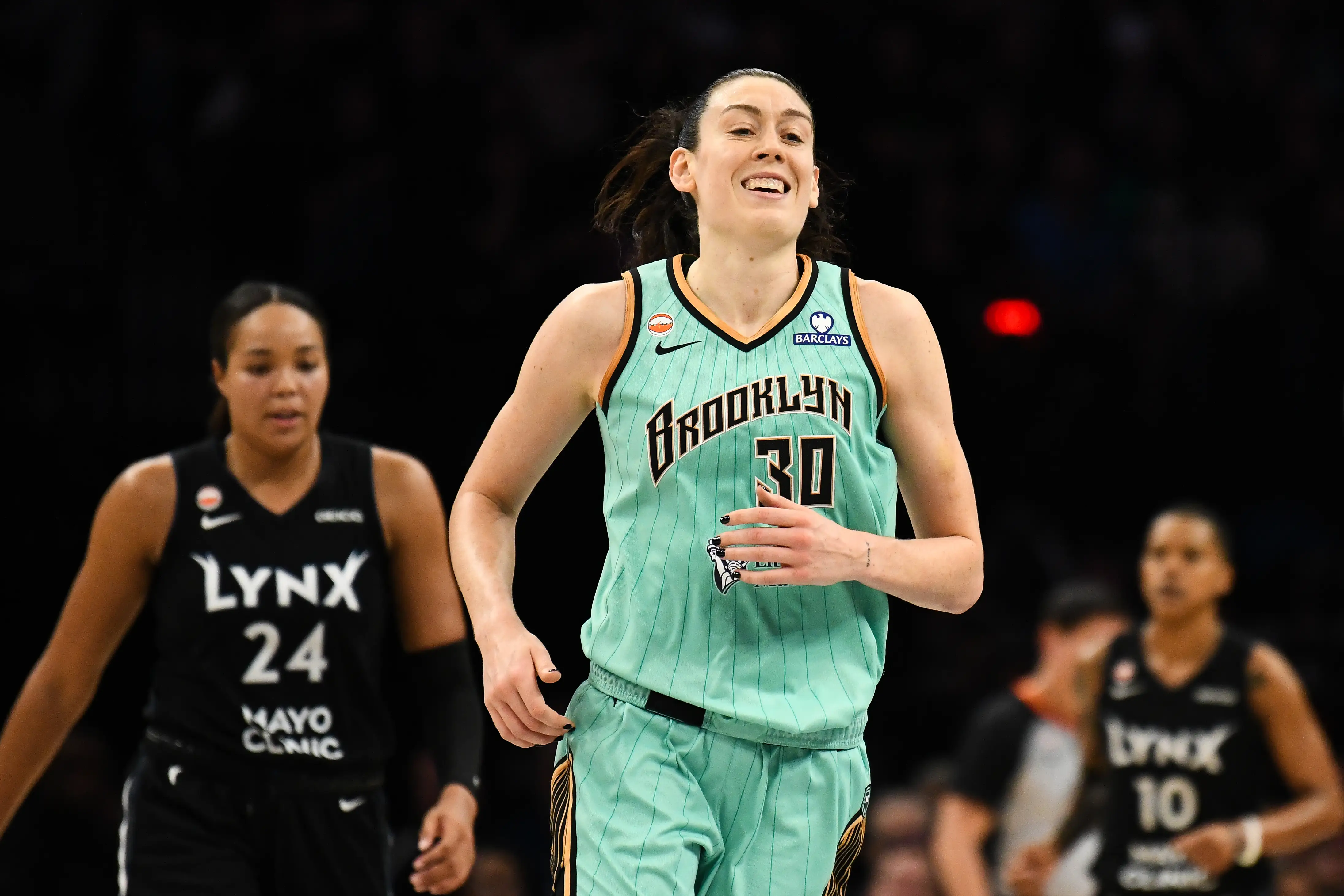 Breanna Stewart in a mint Brooklyn basketball uniform runs on court between Minnesota Lynx players during a game.