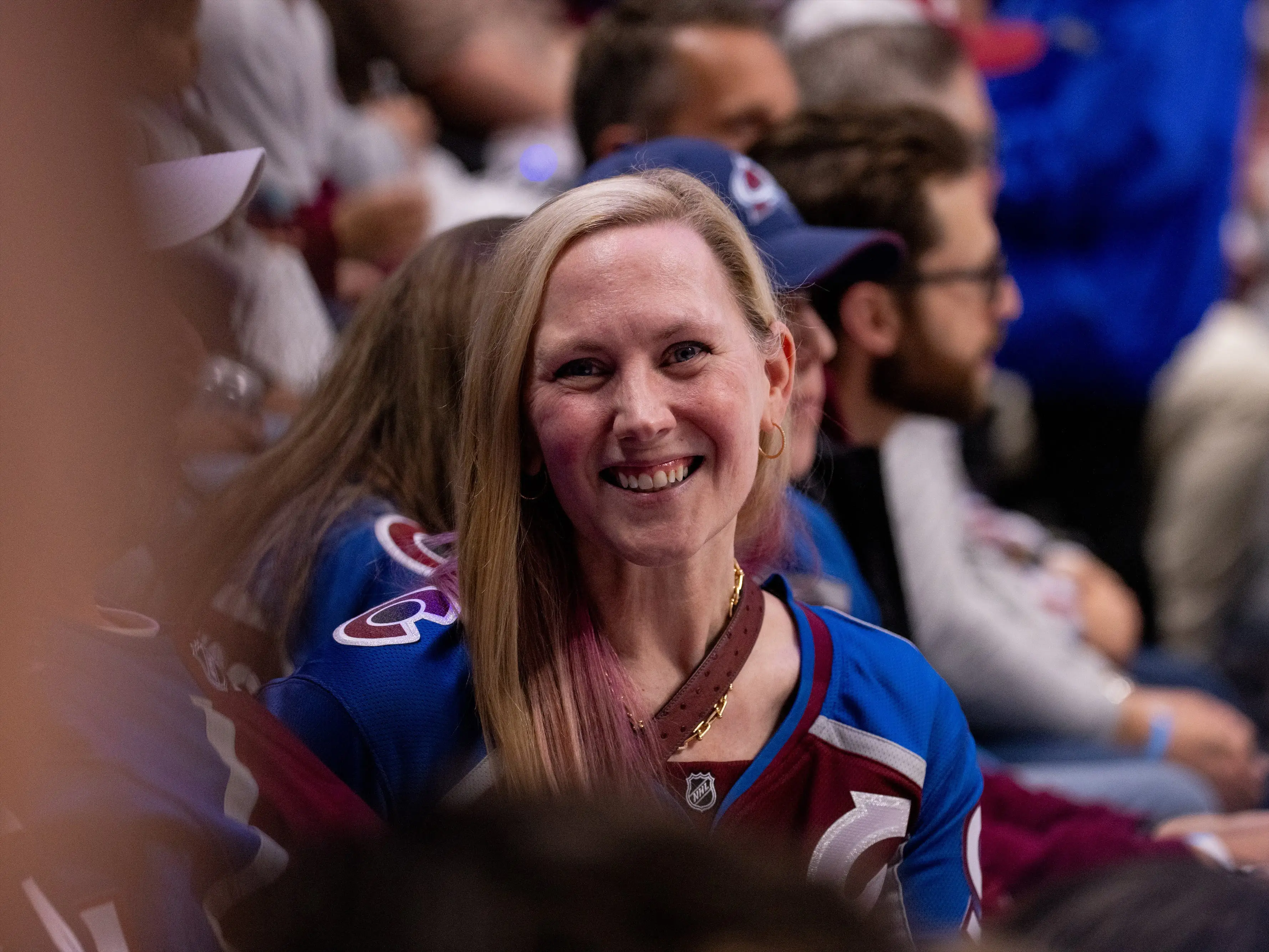 A smiling Colorado Avalanche fan sits among spectators at an indoor hockey game.