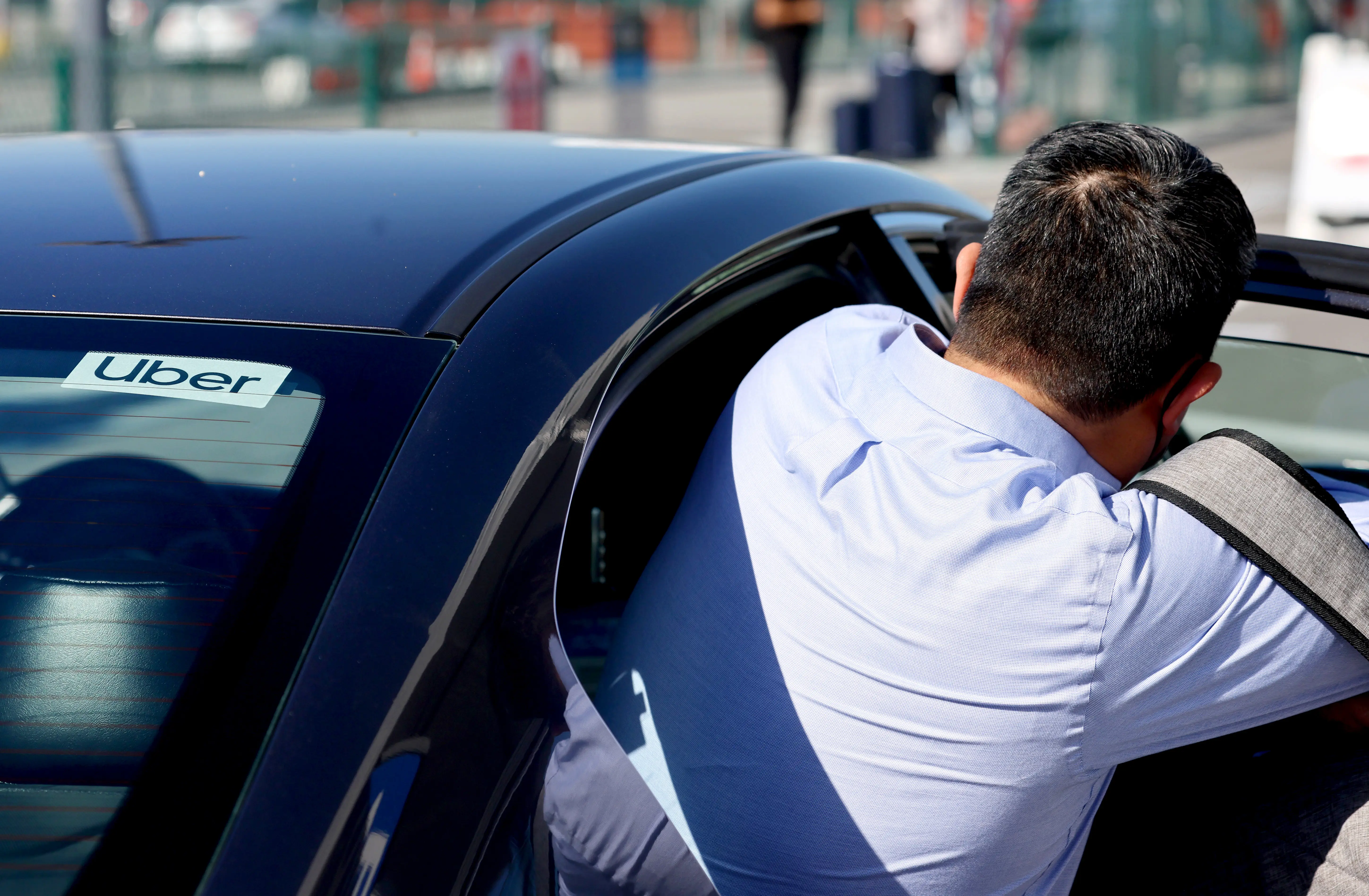 Person leaning into the open rear door of a black car with an “Uber” sign visible in the window.