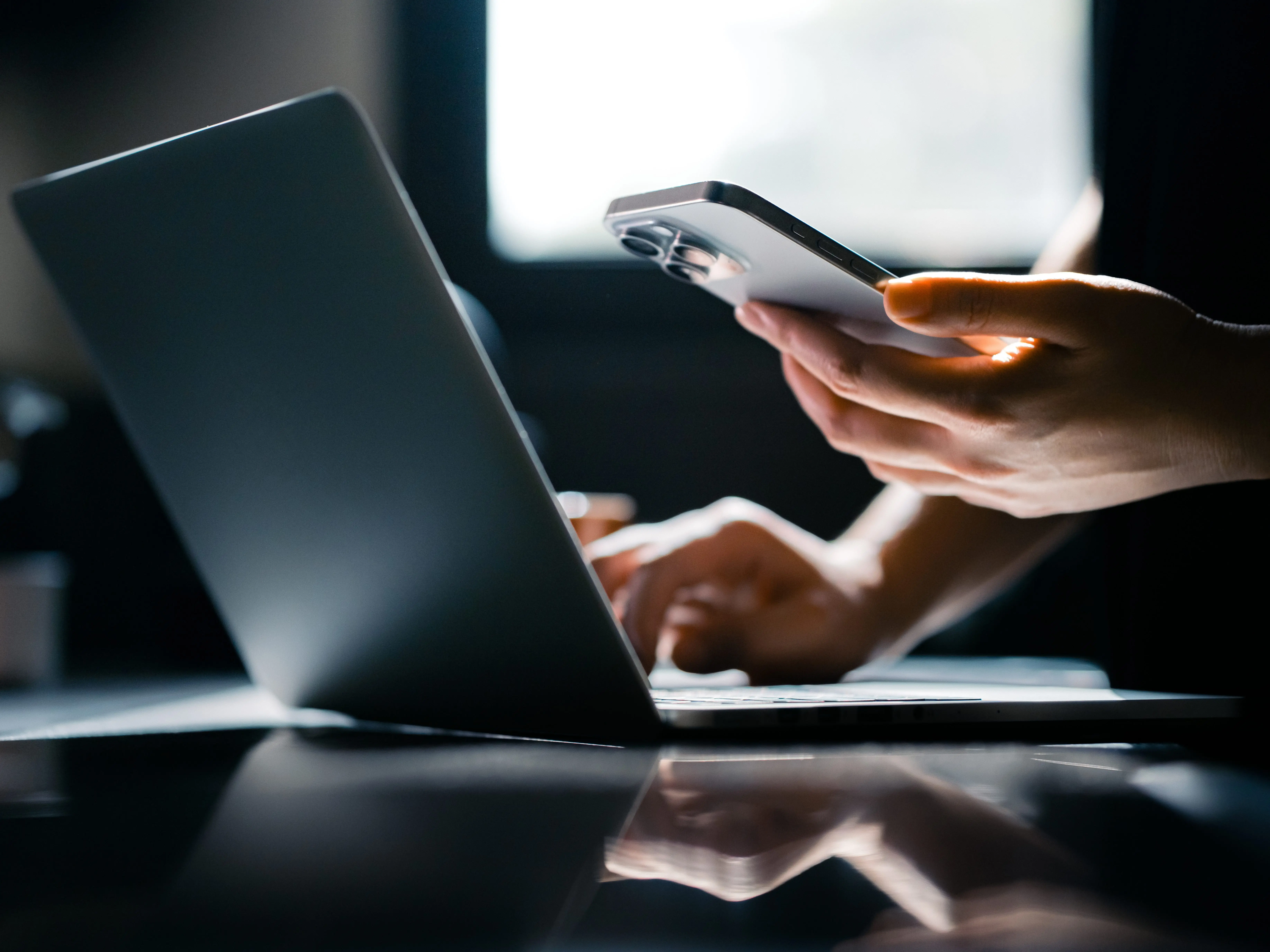 Person using a computer and holding a phone