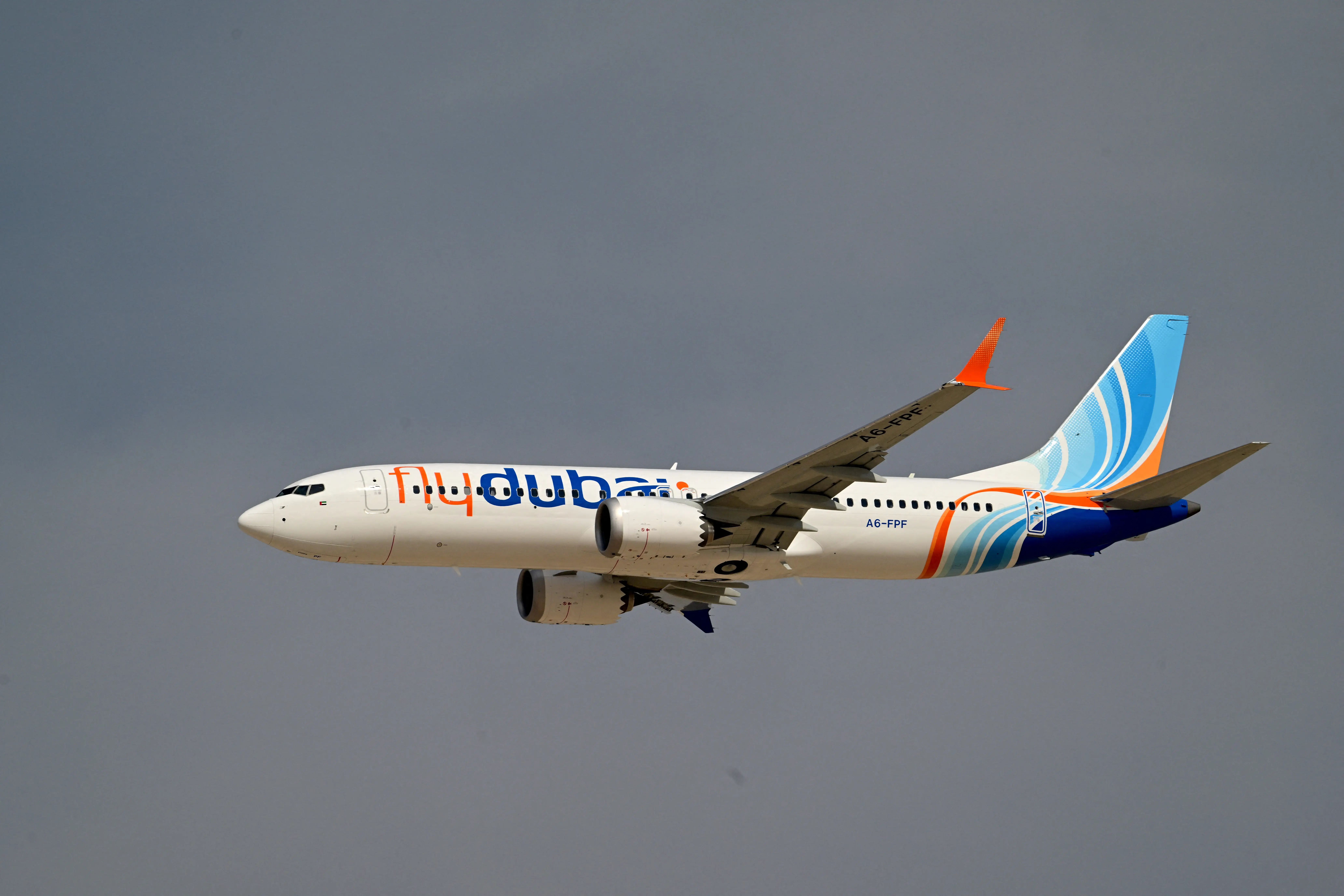 A Flydubai Boeing 737 Max 8  in flight against a gray sky.
