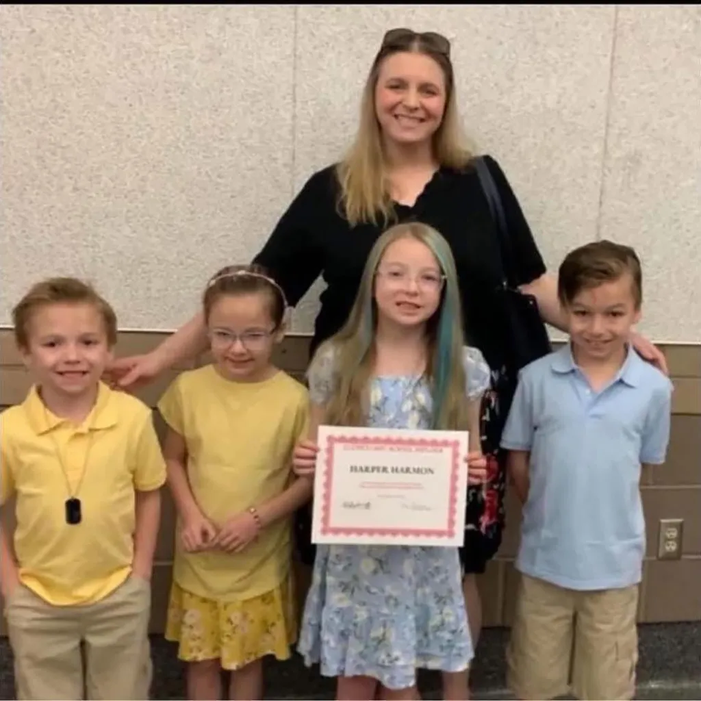 A woman stands behind four smiling children, one of whom holds a certificate that reads 
