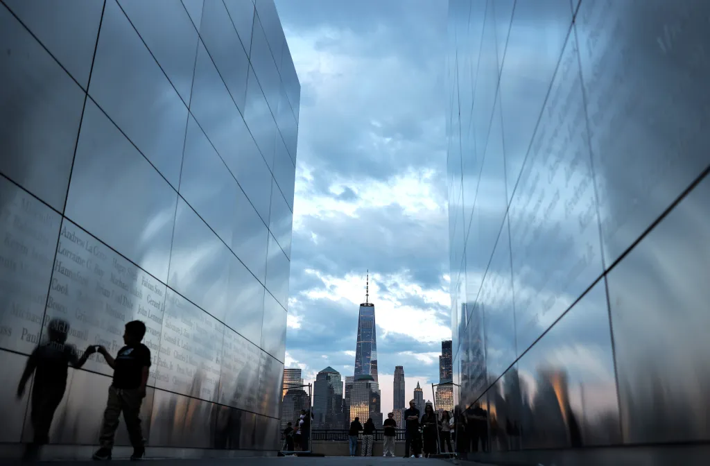 A child walks through the Empty Sky 9/11 Memorial with One World Trade Center and Lower Manhattan in the distance.