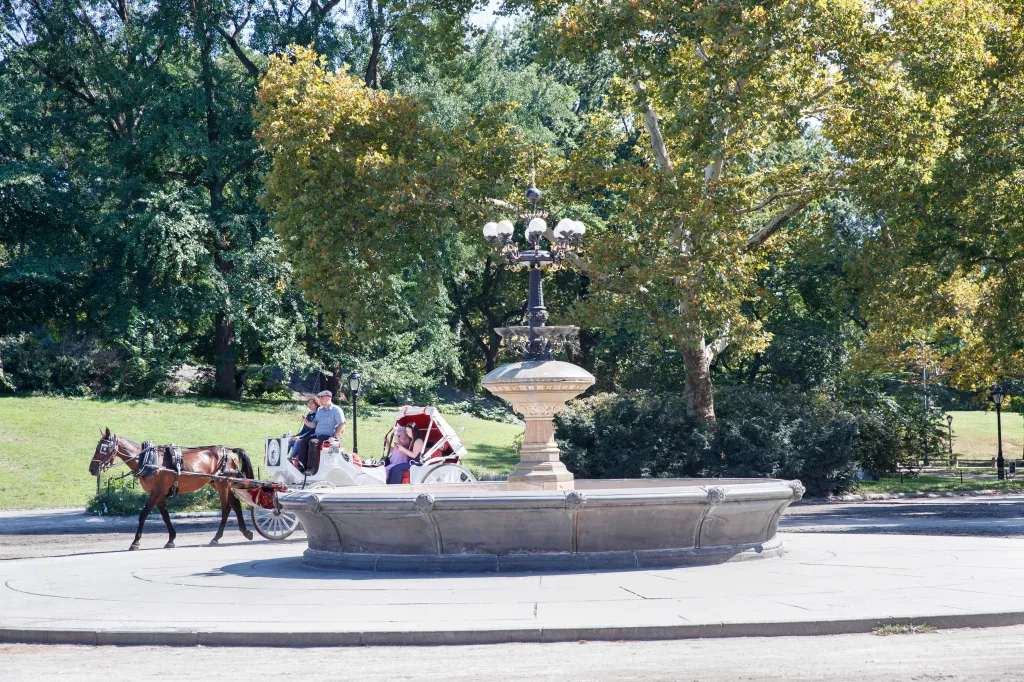 The Cherry Hill horse trough and a horse-drawn carriage with passengers in Central Park.